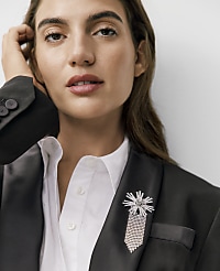 A woman wearing a black blazer with a sparkling brooch and a white shirt poses against a plain white background. carousel Product Image 2