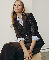A blonde woman wearing a brown velvet suit and light blue shirt sits against a plain white wall. carousel Product Image 5