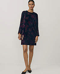 A woman wearing a short, long-sleeved black velvet dress and black heels stands against a plain white background. carousel Product Image 1