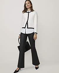 A woman wearing a white tweed jacket, white shirt, and black leather flared trousers stands against a plain white background while holding a black handbag. carousel Product Image 1
