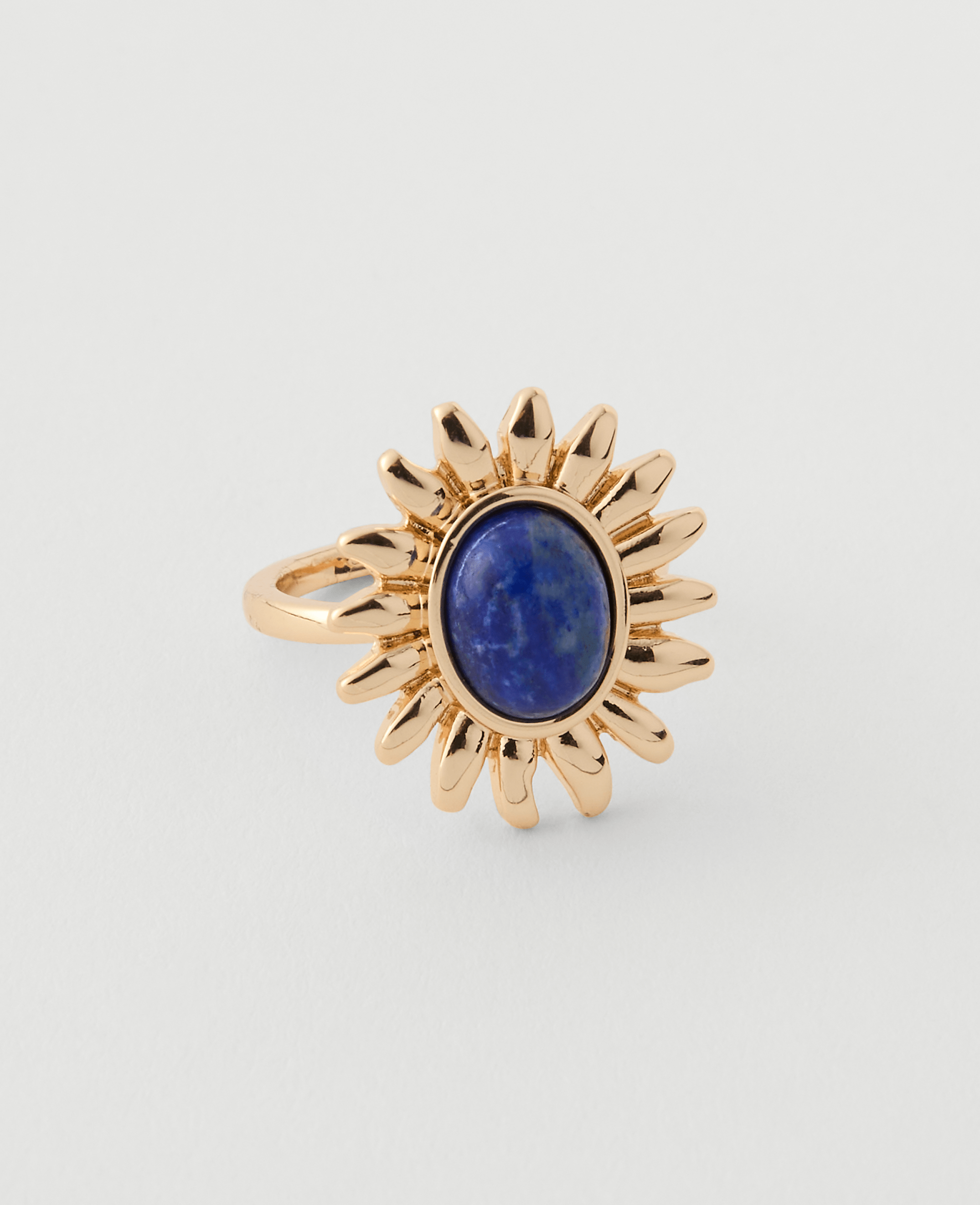 A gold ring with a sunflower design and a blue stone sits on a plain white background.
