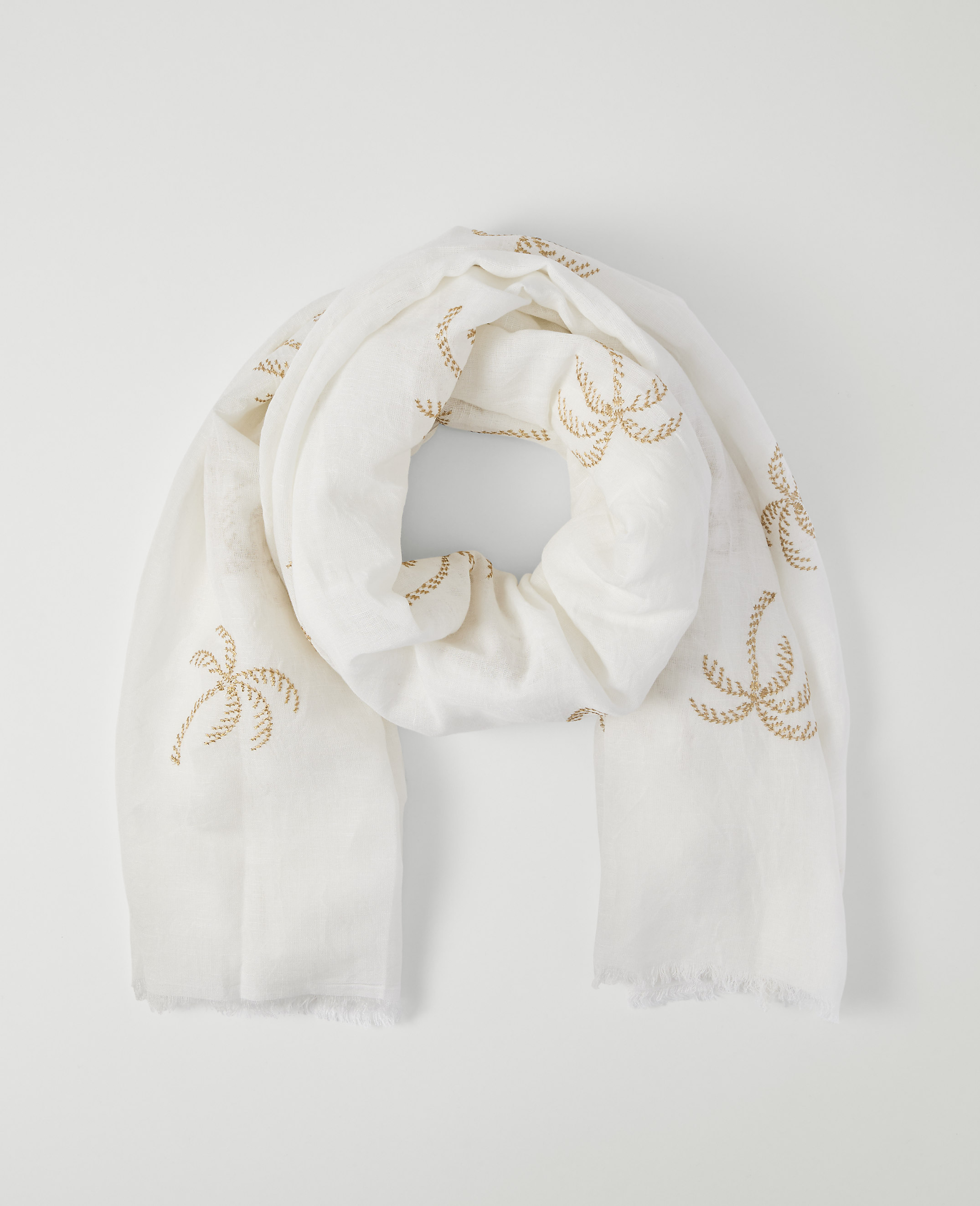 A white scarf with embroidered palm trees is laid out against a plain white background.