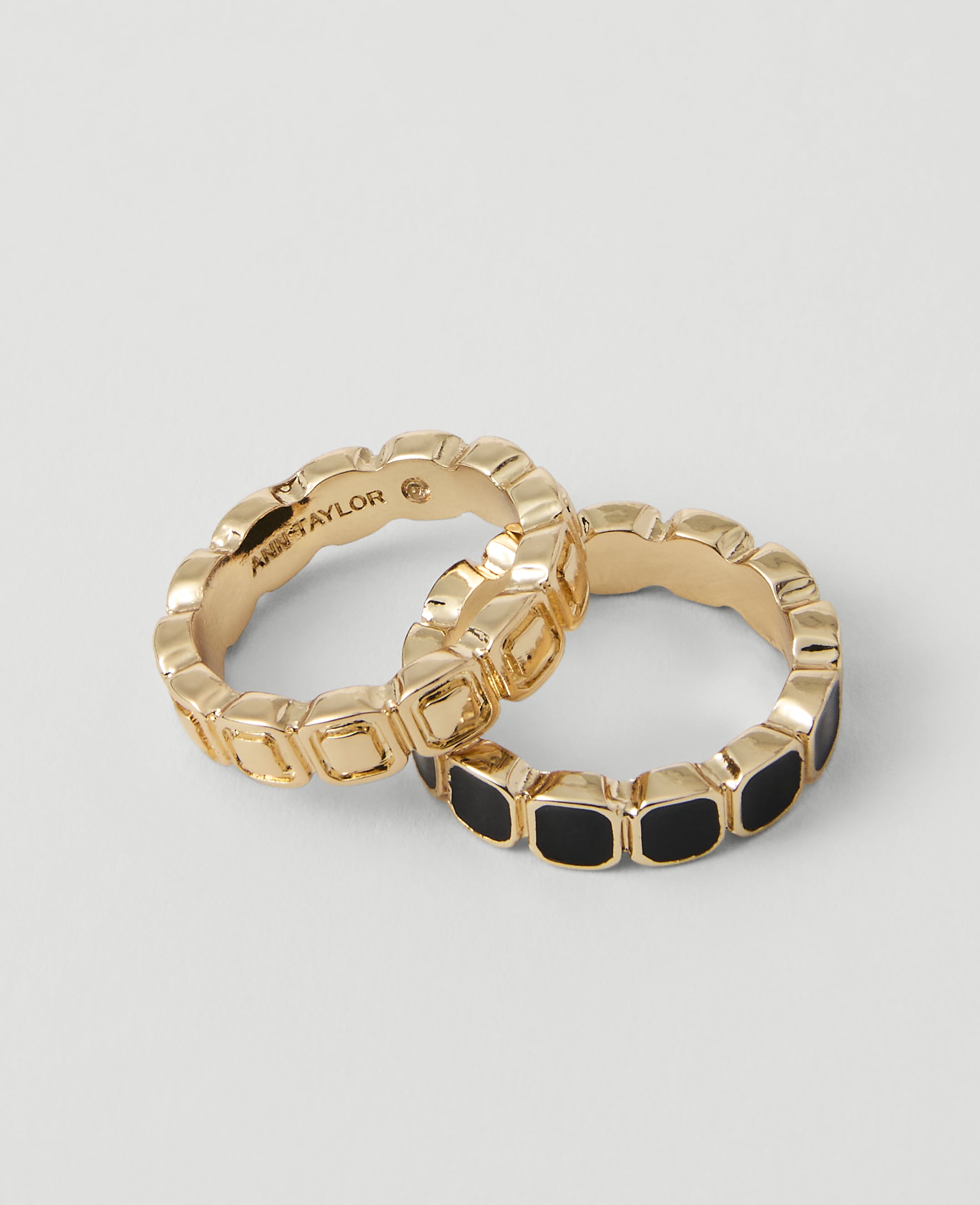 Two gold rings, one with black enamel squares and the other plain, rest on a plain white background.