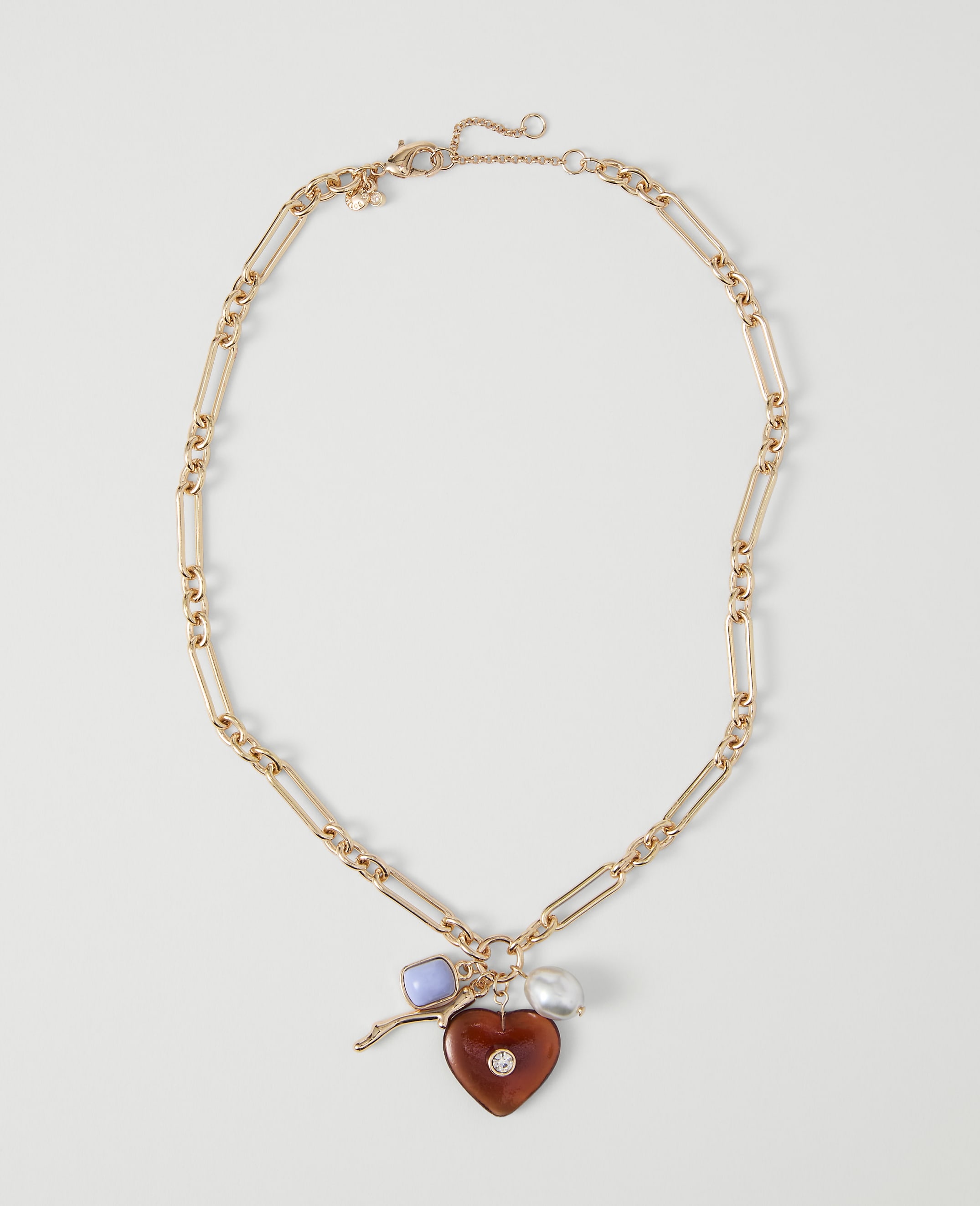 A gold chain necklace with a heart-shaped pendant and charms rests on a plain white background.