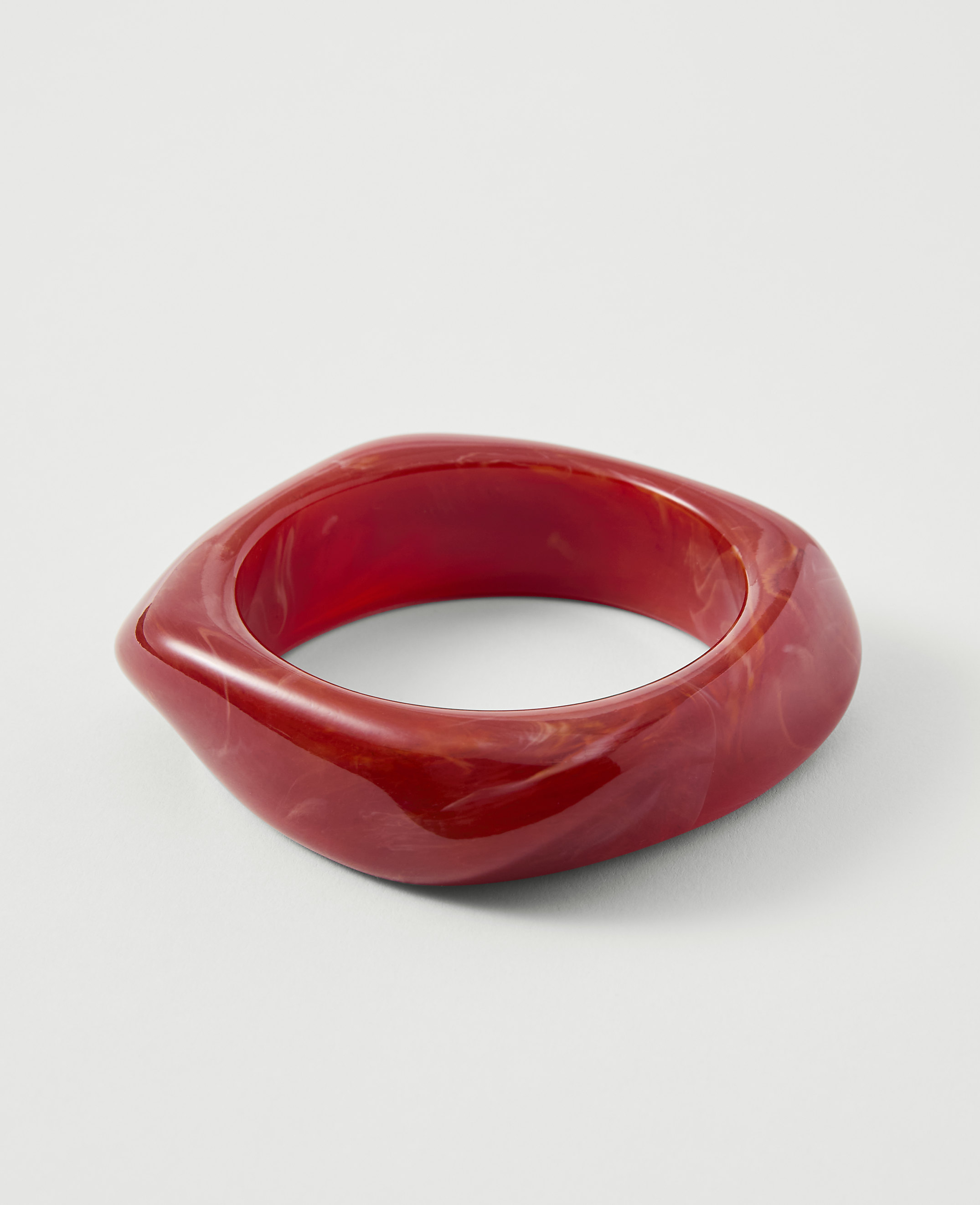 A red, swirled resin bangle rests on a plain white background.