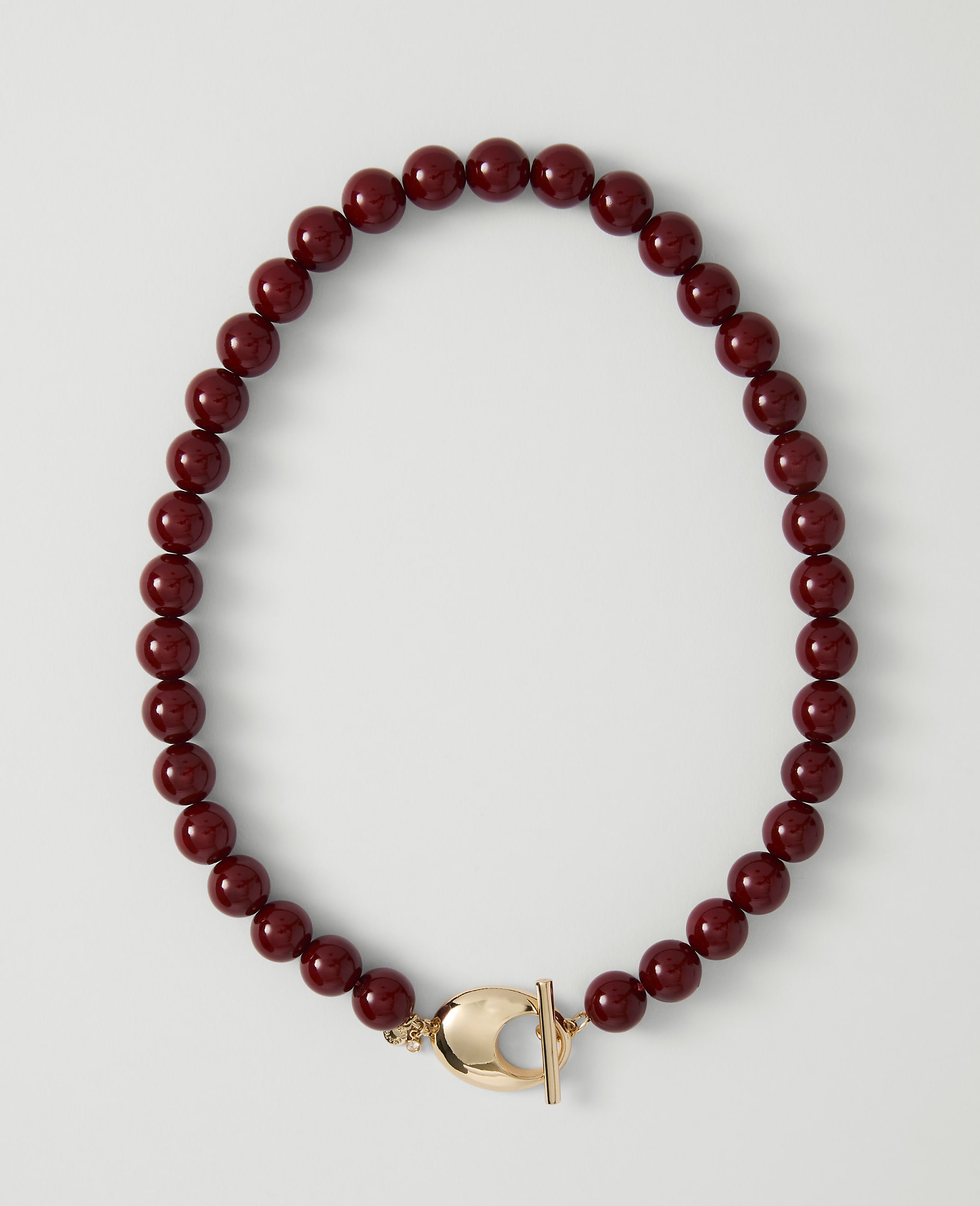 A deep red beaded necklace with a gold clasp lies on a plain white background.