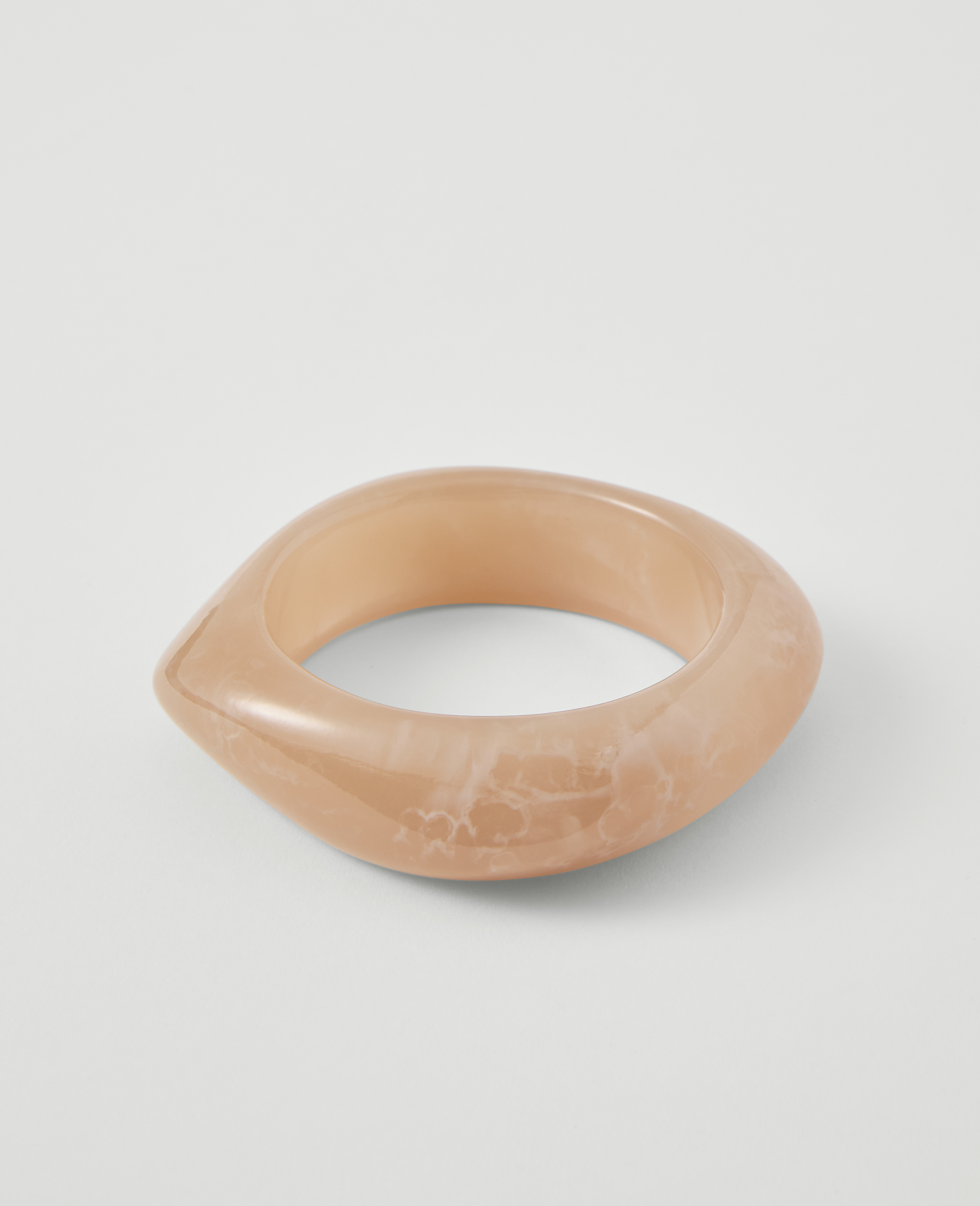 A translucent, peachy-pink bangle with a marbled pattern rests on a plain white background.