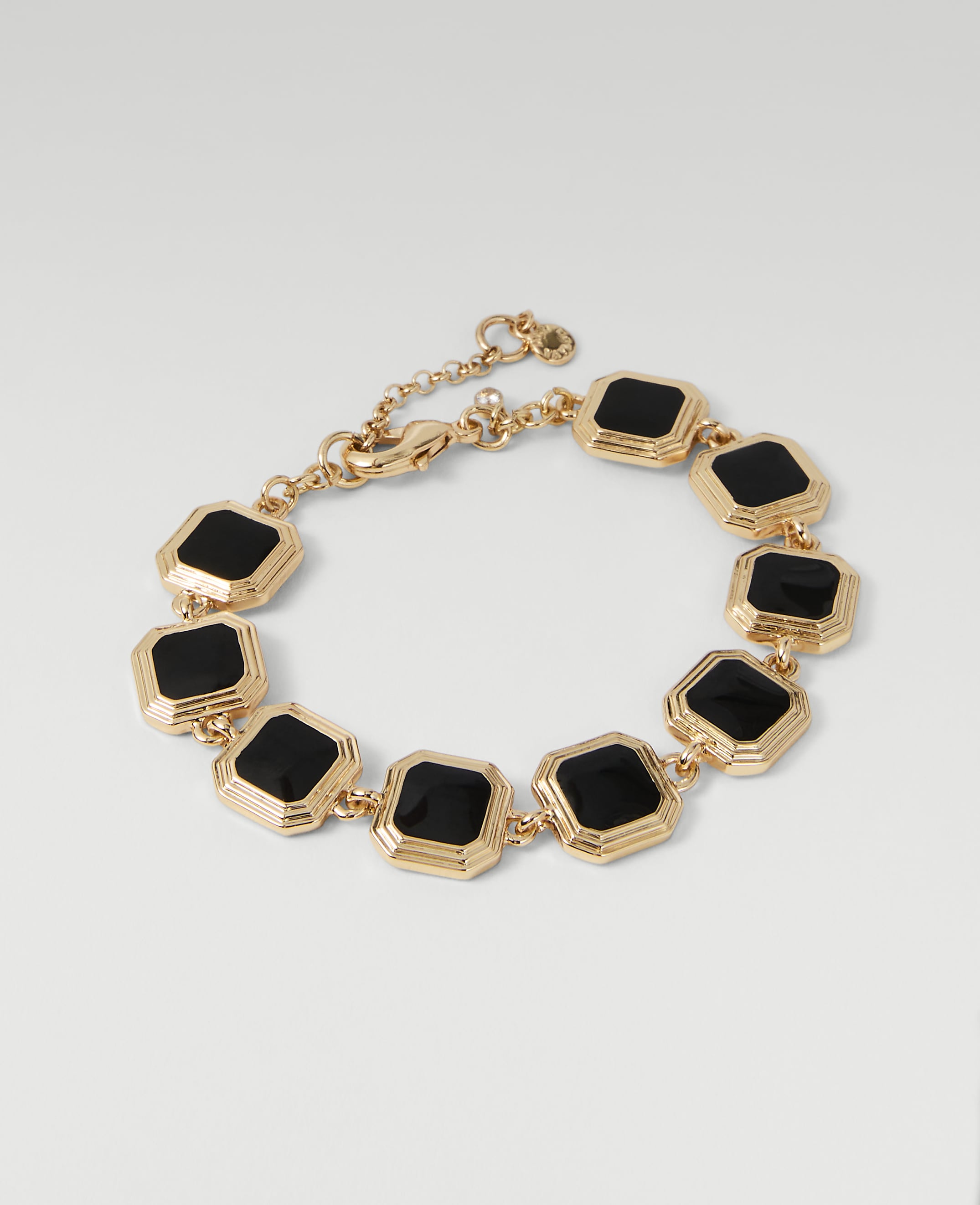 A gold bracelet with black square stones is displayed against a plain white background.