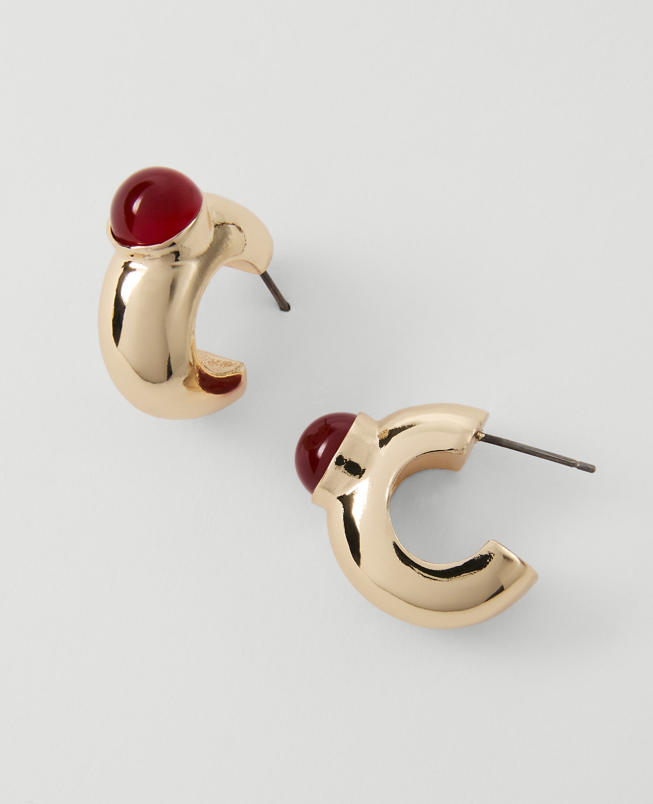 A pair of gold hoop earrings with red gem accents rests on a plain white background.