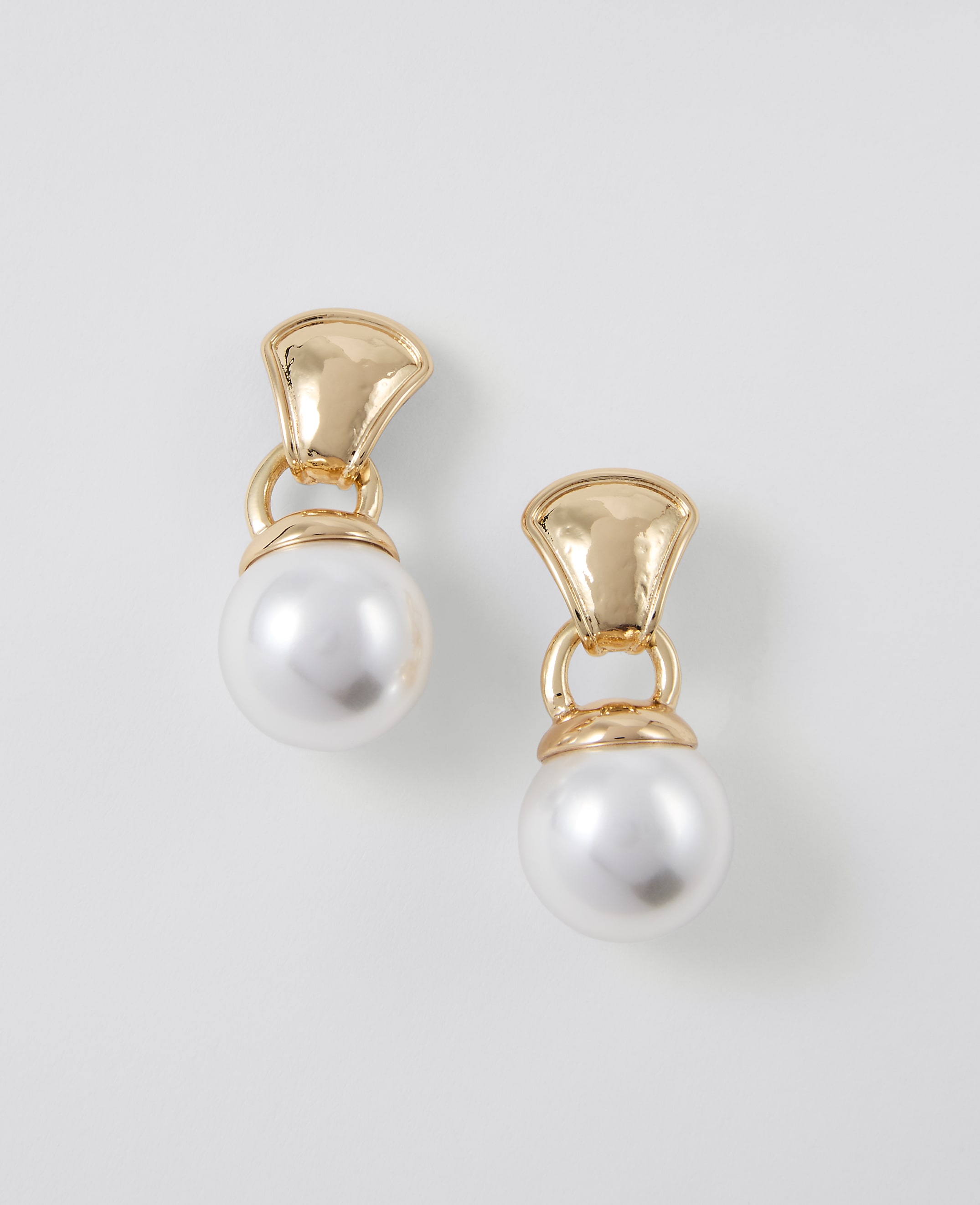 A pair of gold and pearl drop earrings hang against a plain white background.