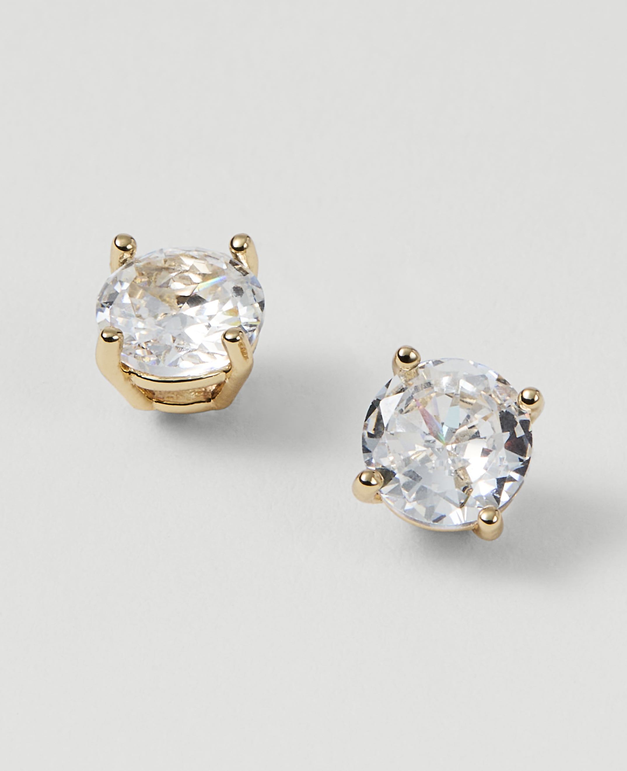 Two sparkling diamond stud earrings with gold settings rest on a plain white background.