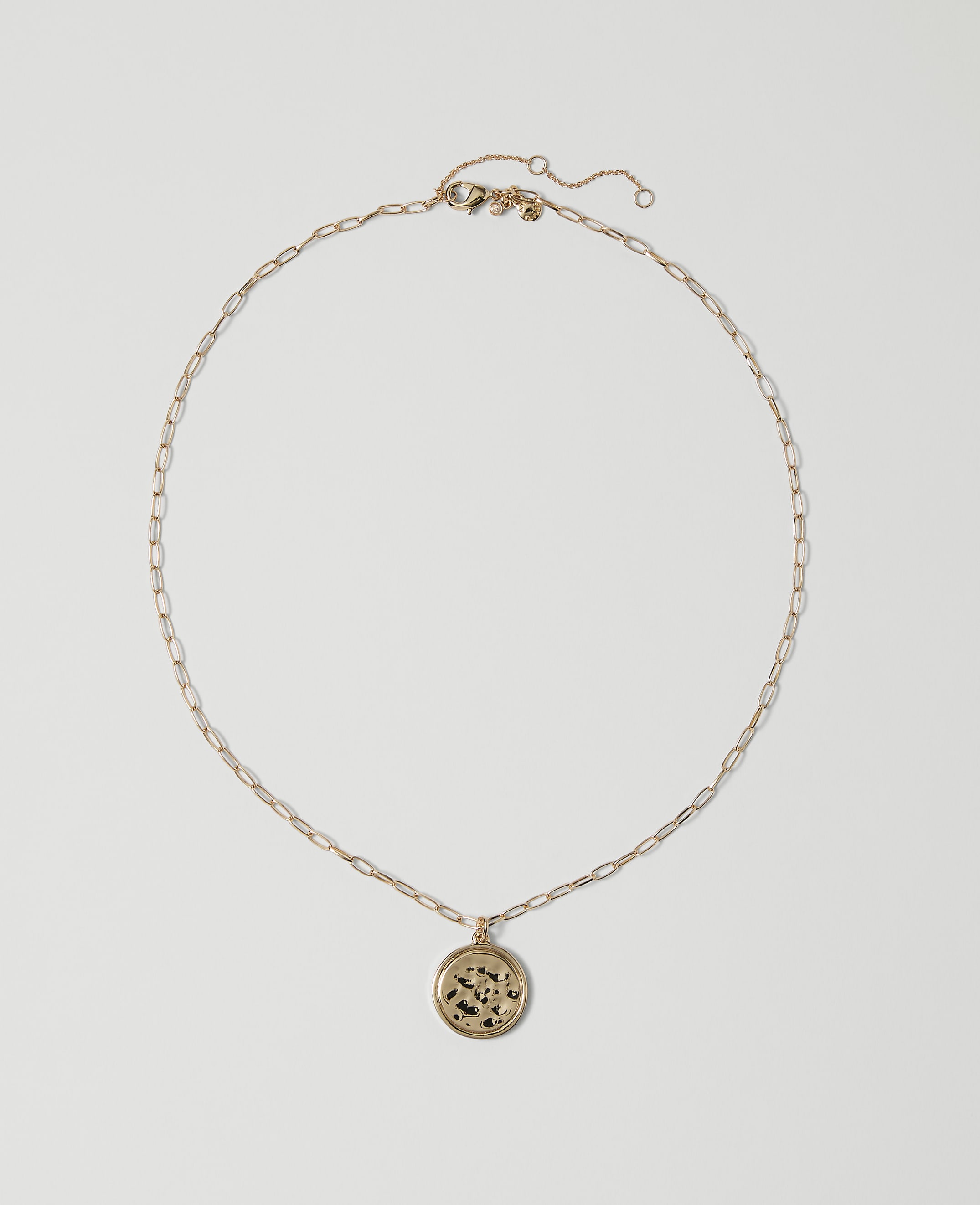 A delicate gold chain necklace with a circular pendant rests on a plain white background.
