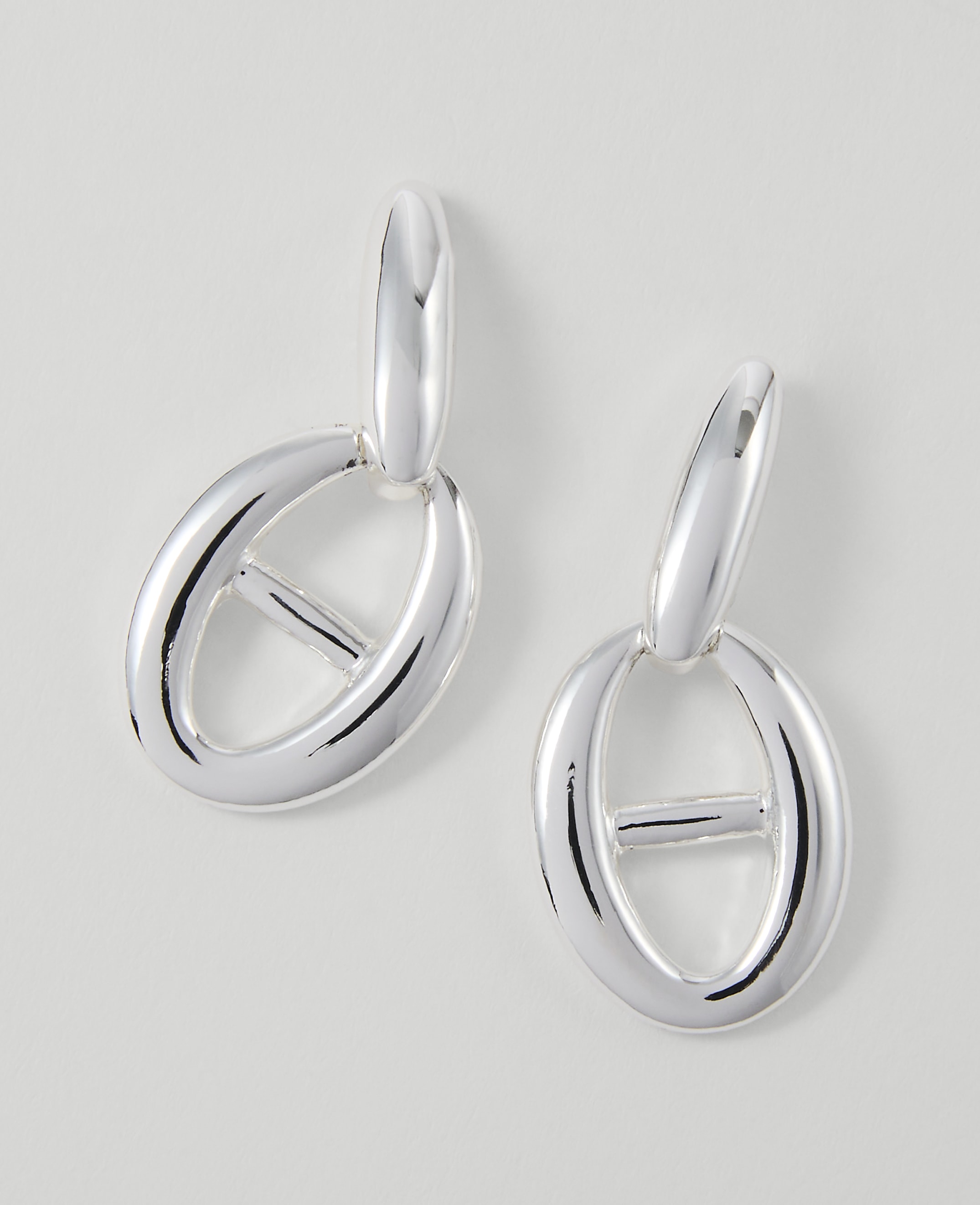 A pair of silver oval link earrings hang against a plain white background.