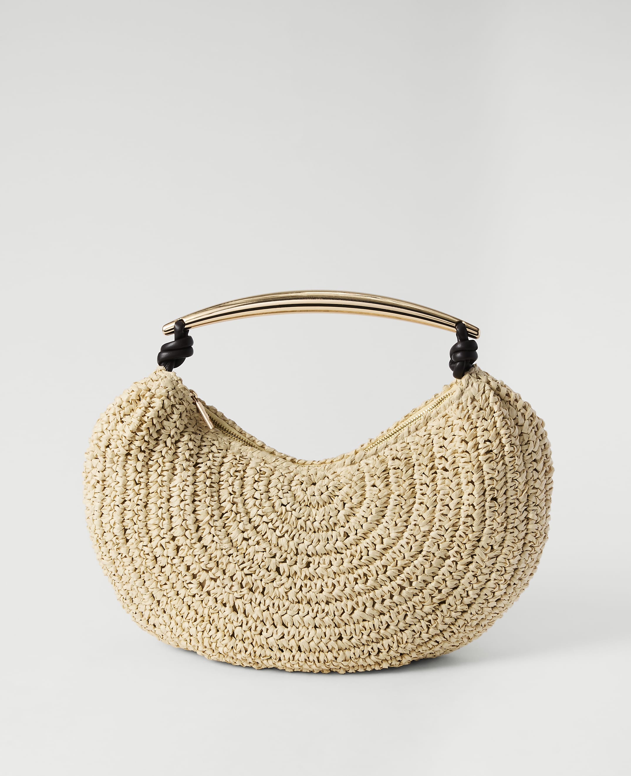 A beige crocheted crescent-shaped handbag with a gold curved handle rests against a plain white background.