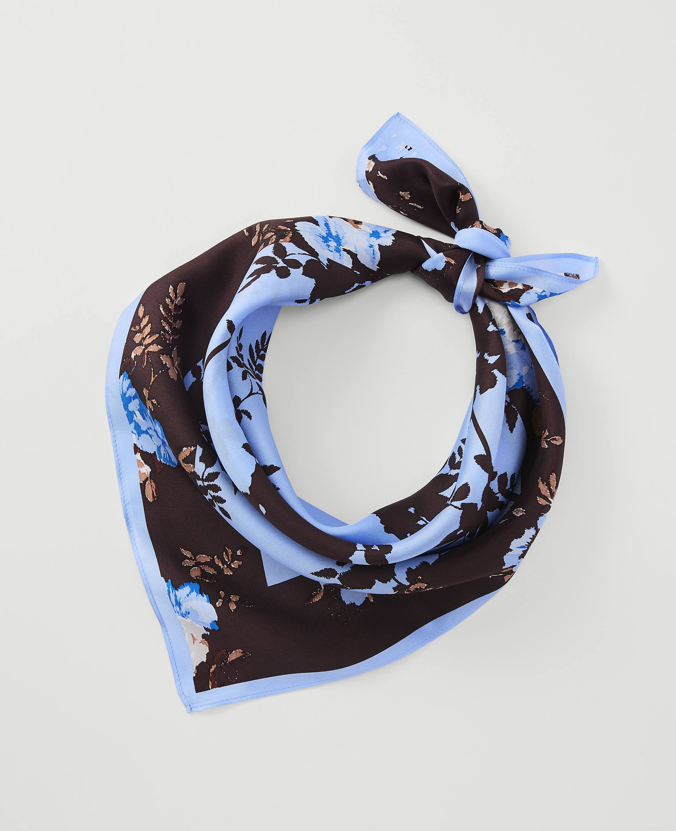 A light blue and brown floral patterned silk scarf is tied in a knot against a plain white background.