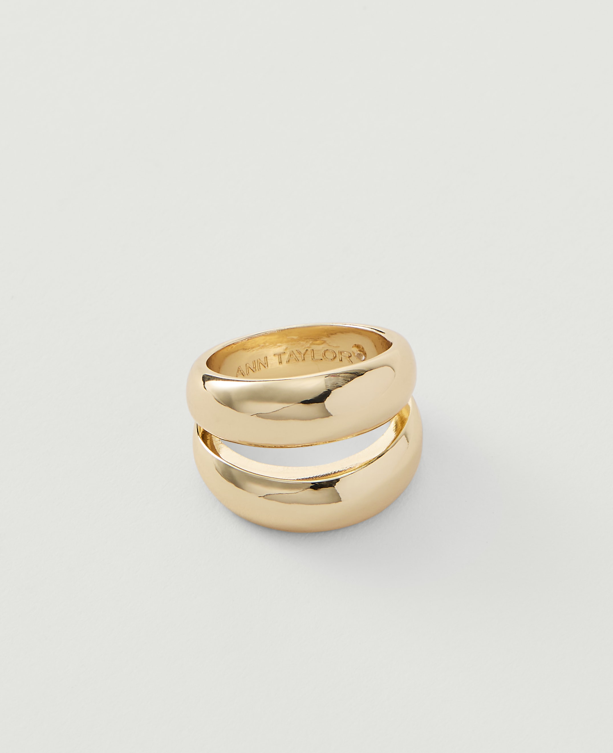 Two stacked gold rings with "ANN TAYLOR" inscribed on the inner surface rest on a plain white background.