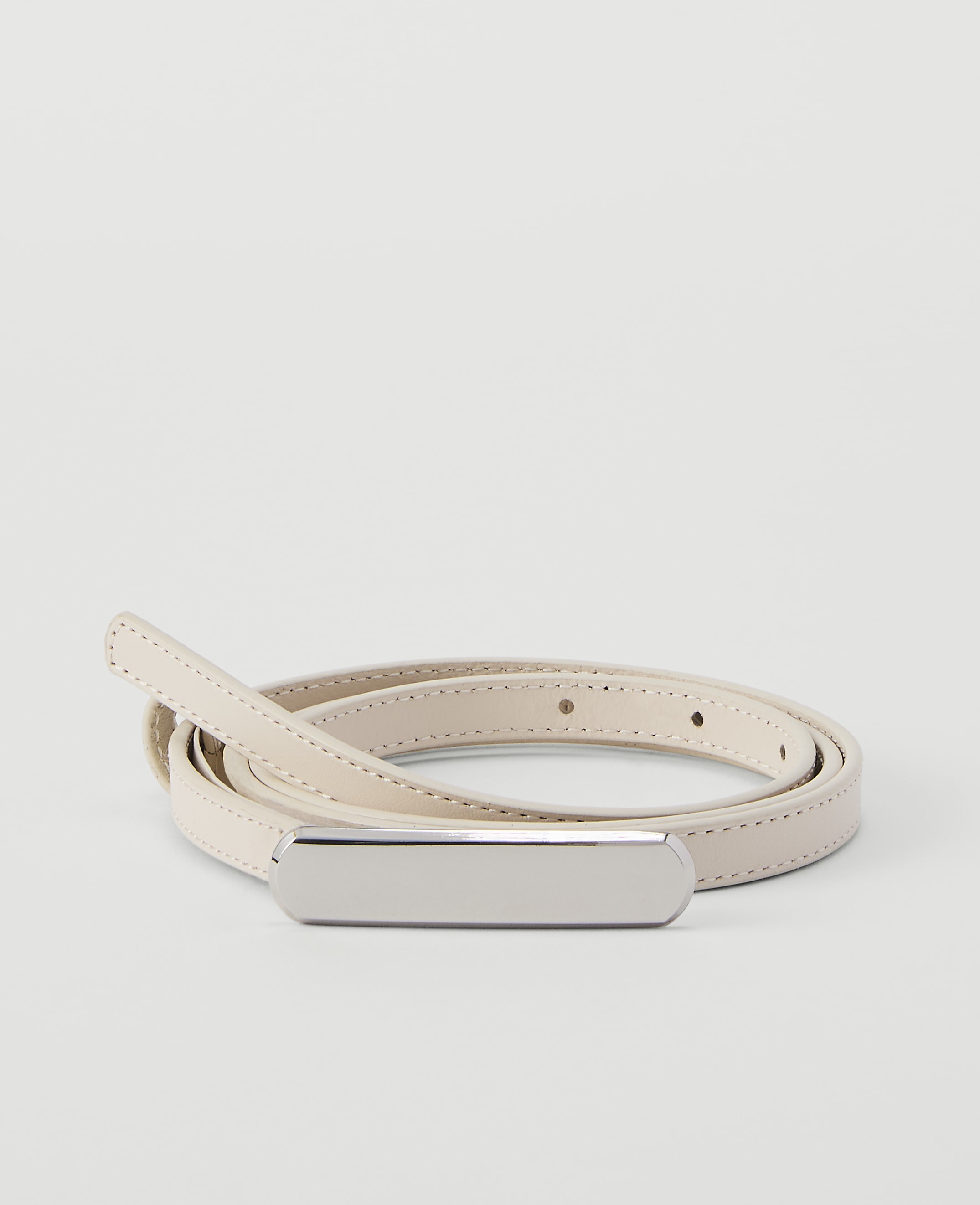A thin, cream-colored leather belt with a silver buckle lies coiled on a plain, light gray background.