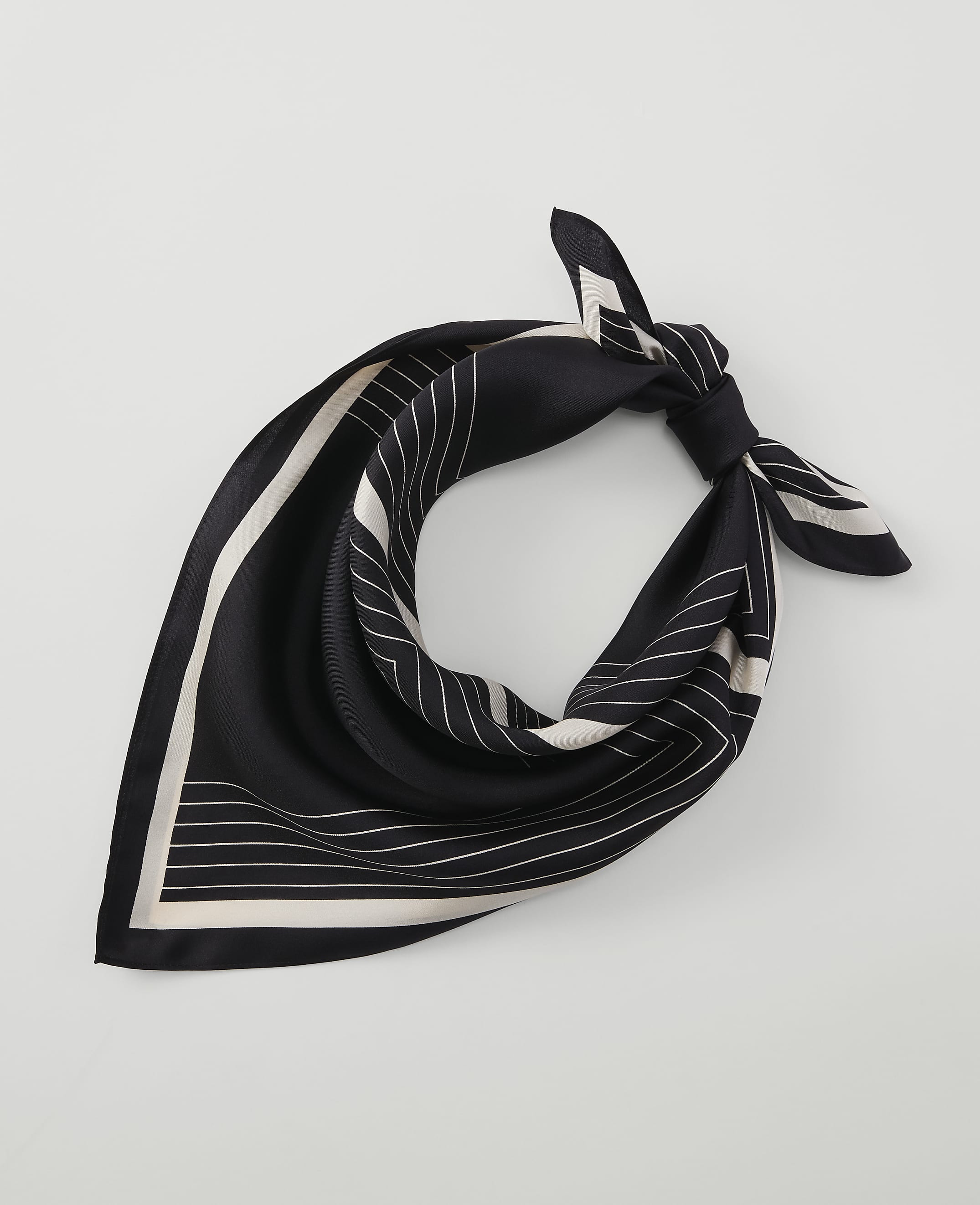 A black silk scarf with white geometric lines is tied in a knot against a plain white background.