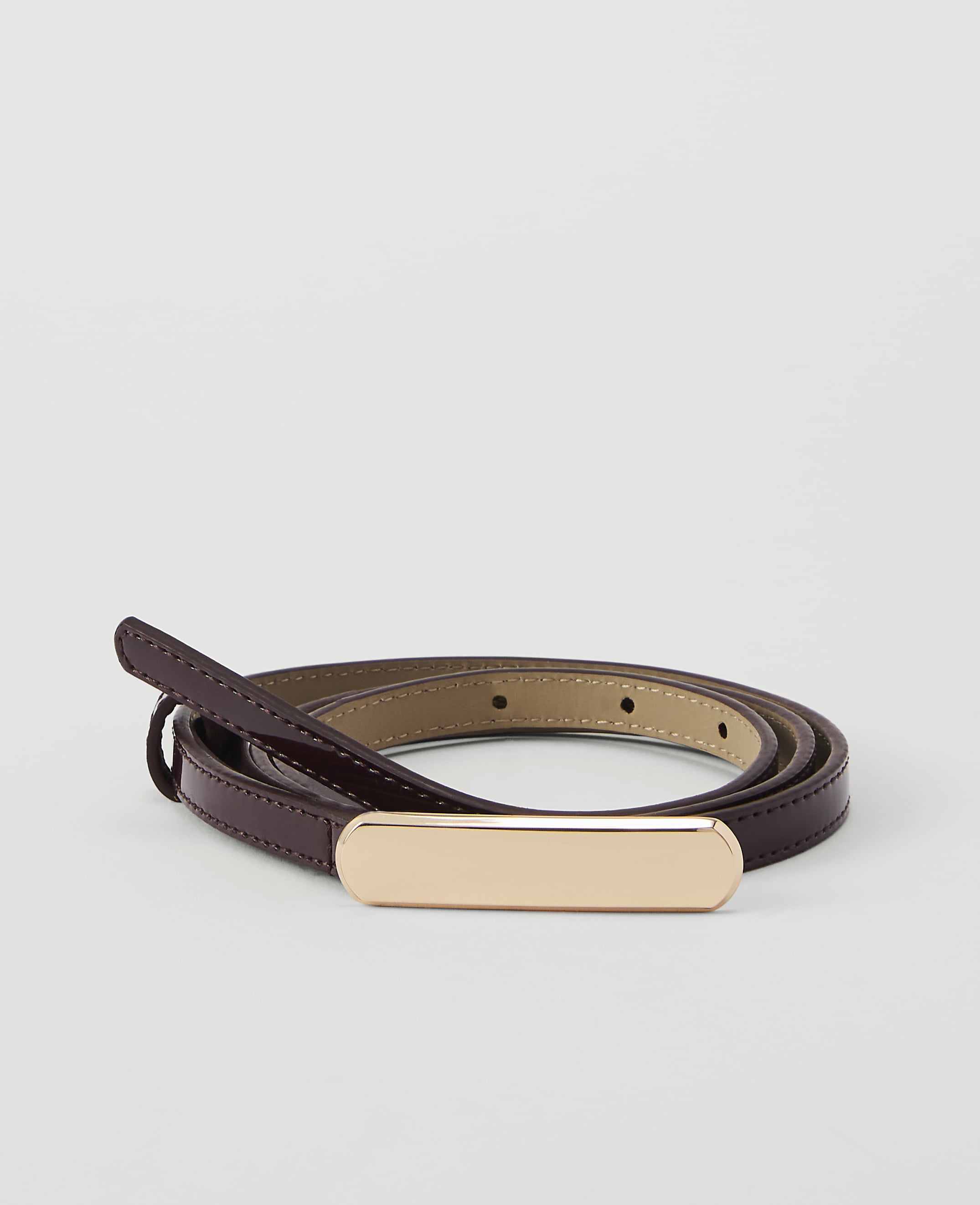 A thin, dark red patent leather belt with a gold buckle is coiled on a plain white background.