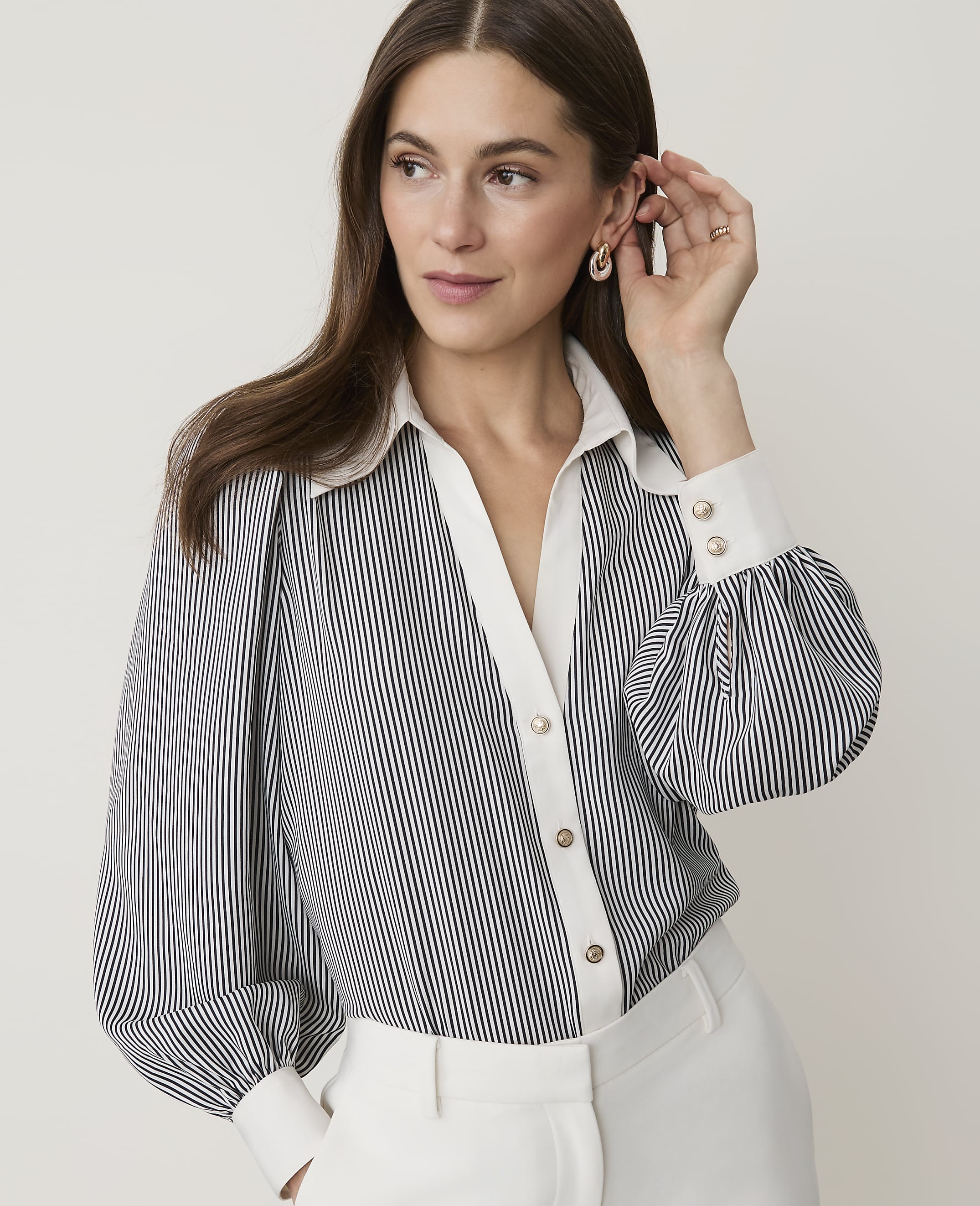 A woman in a striped blouse with puffed sleeves and white collar and cuffs poses against a plain, light background.