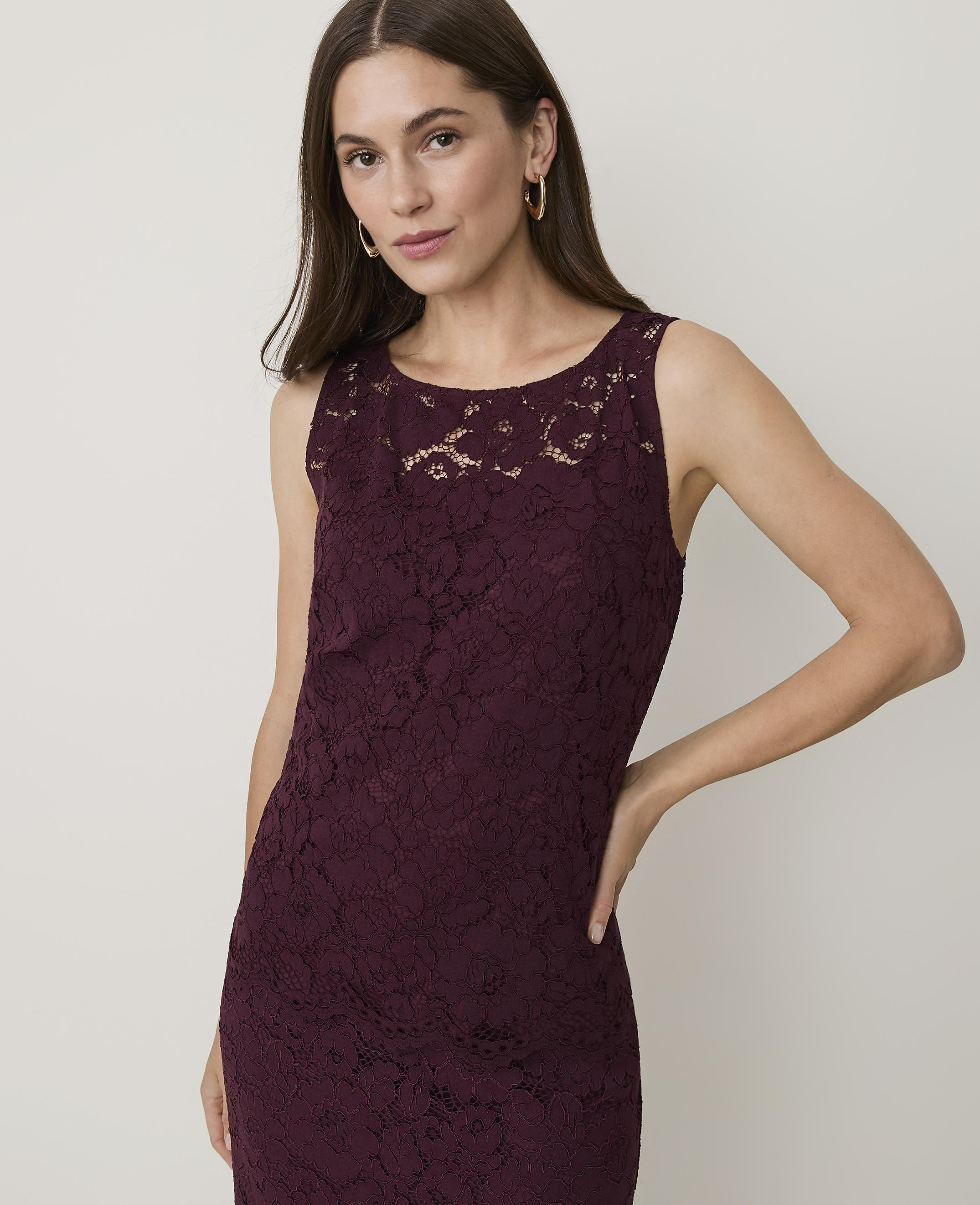 A woman in a burgundy lace dress stands against a plain, light-colored background.