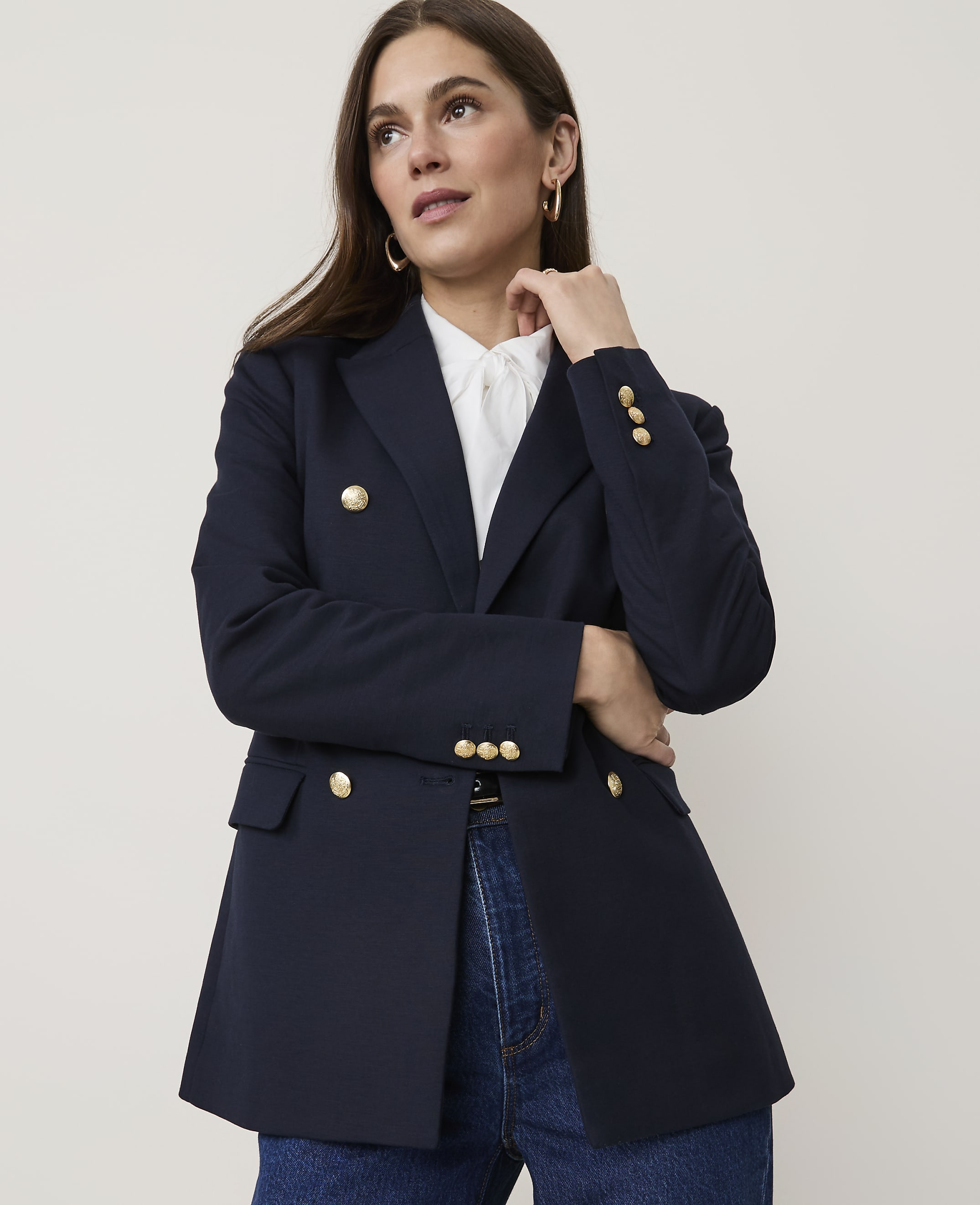 A woman in a navy blazer and jeans poses against a plain, light-colored background.