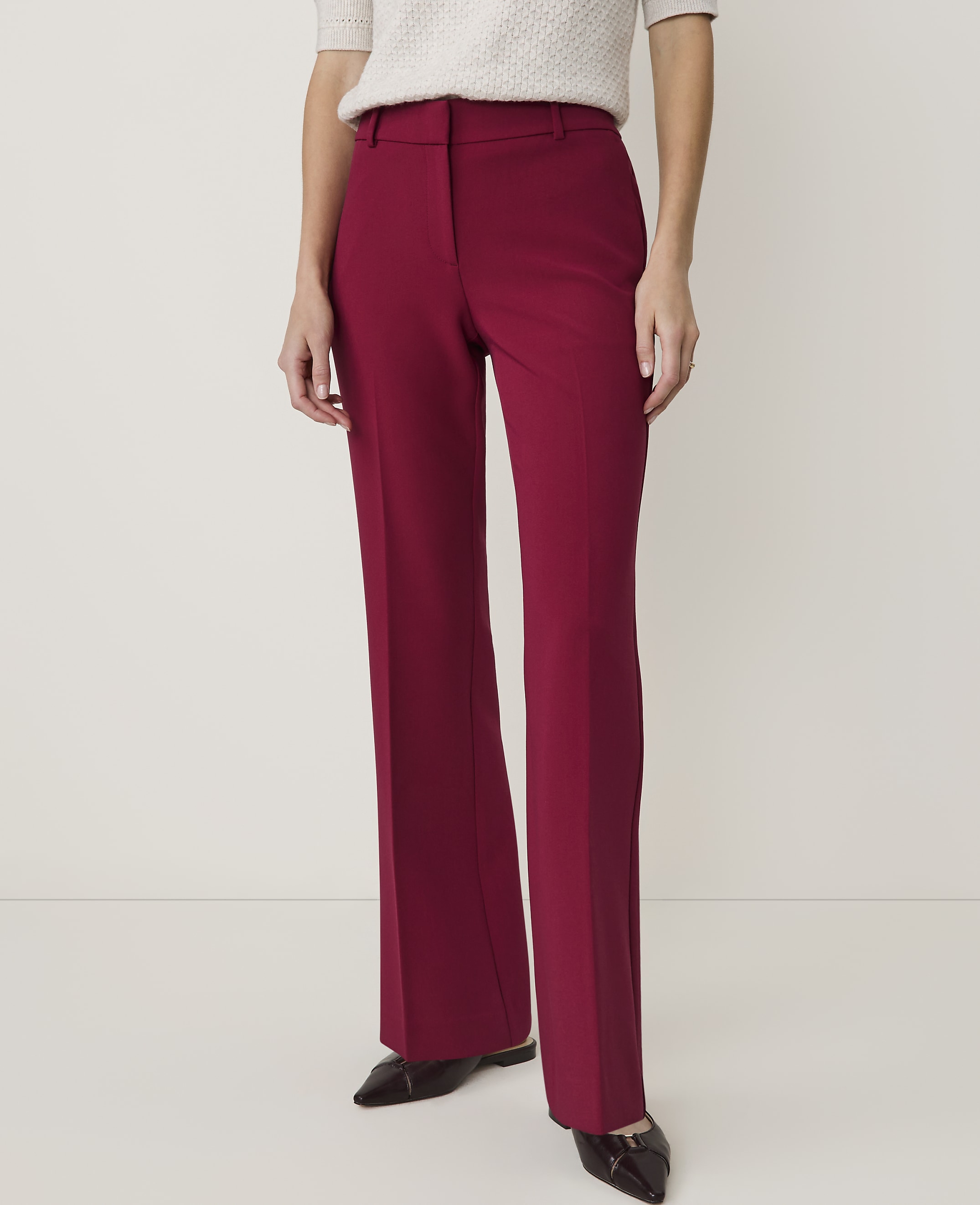 A person in burgundy flared trousers and a cream-colored top stands against a plain white background.