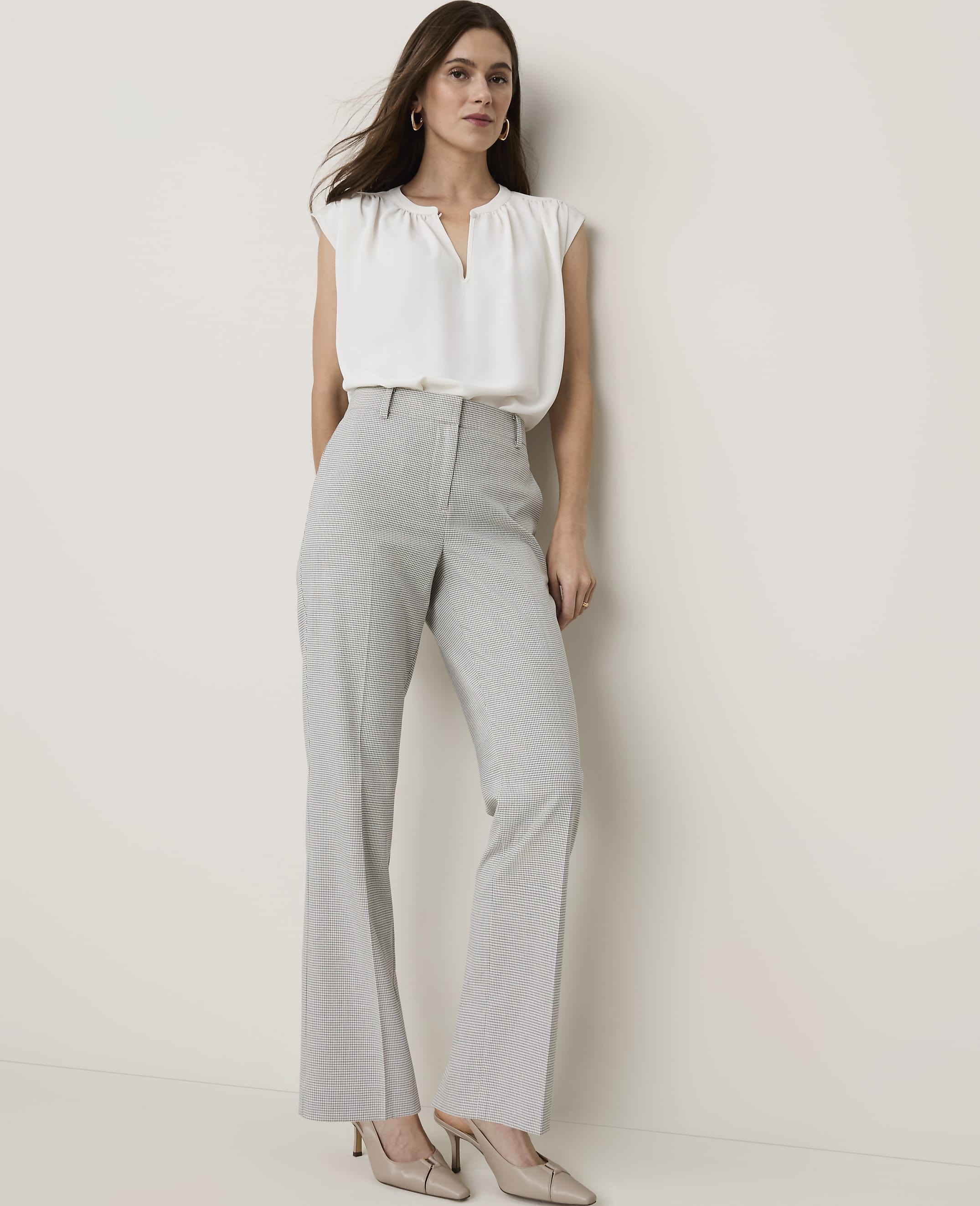A woman in a white blouse and checkered pants stands against a plain white background.