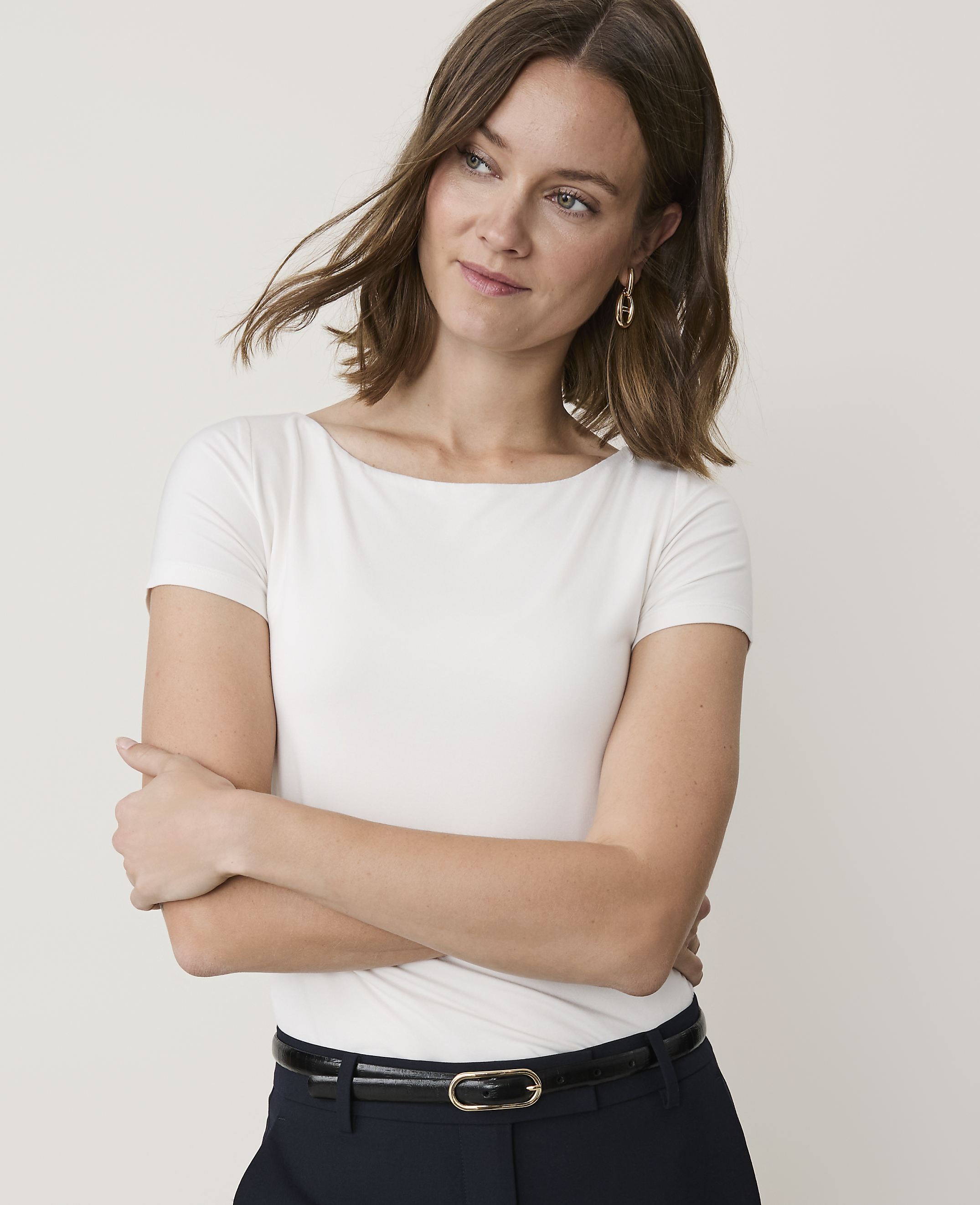 A woman in a white t-shirt and dark pants stands against a plain background.