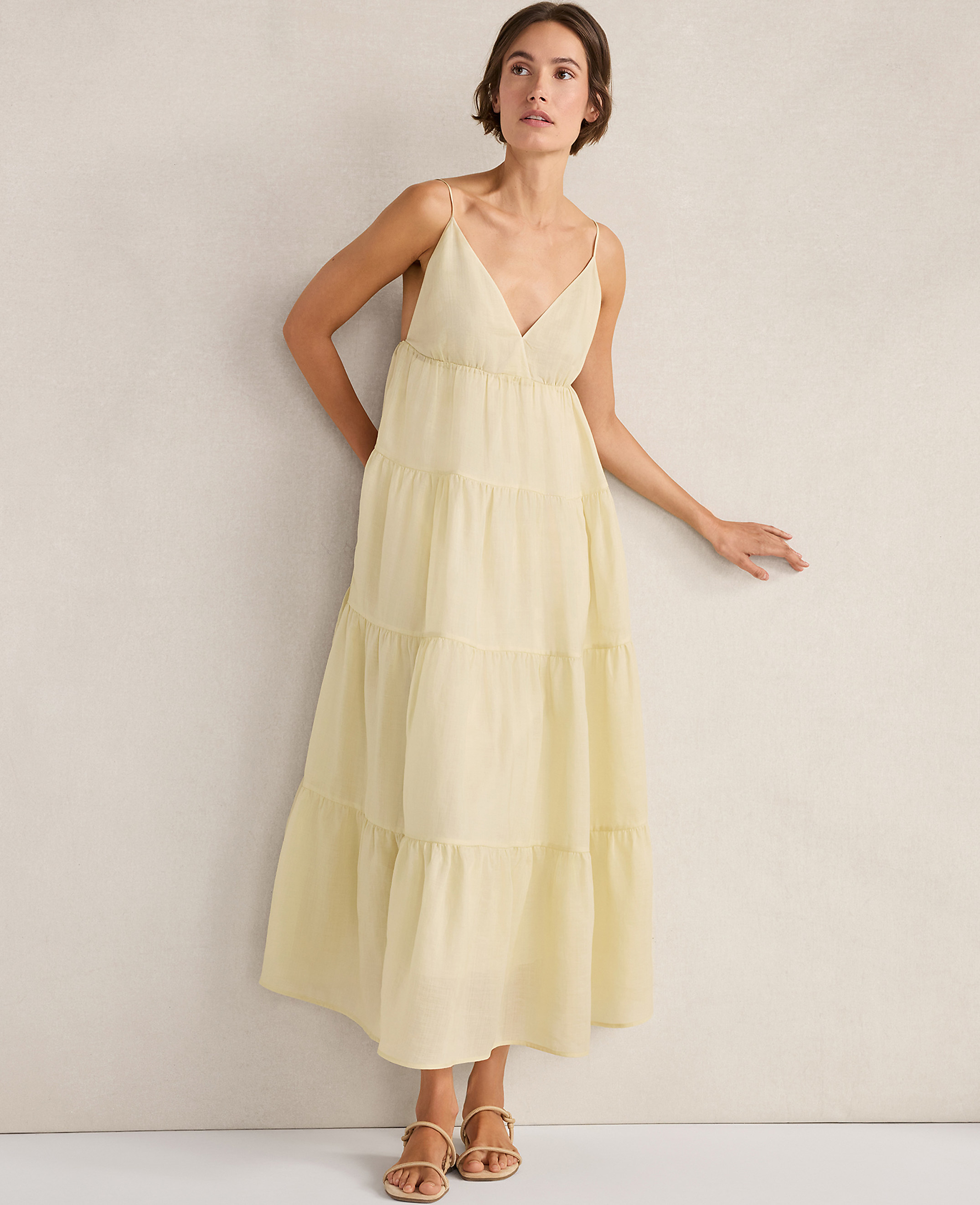 A woman in a flowing yellow tiered dress stands against a plain, textured wall.