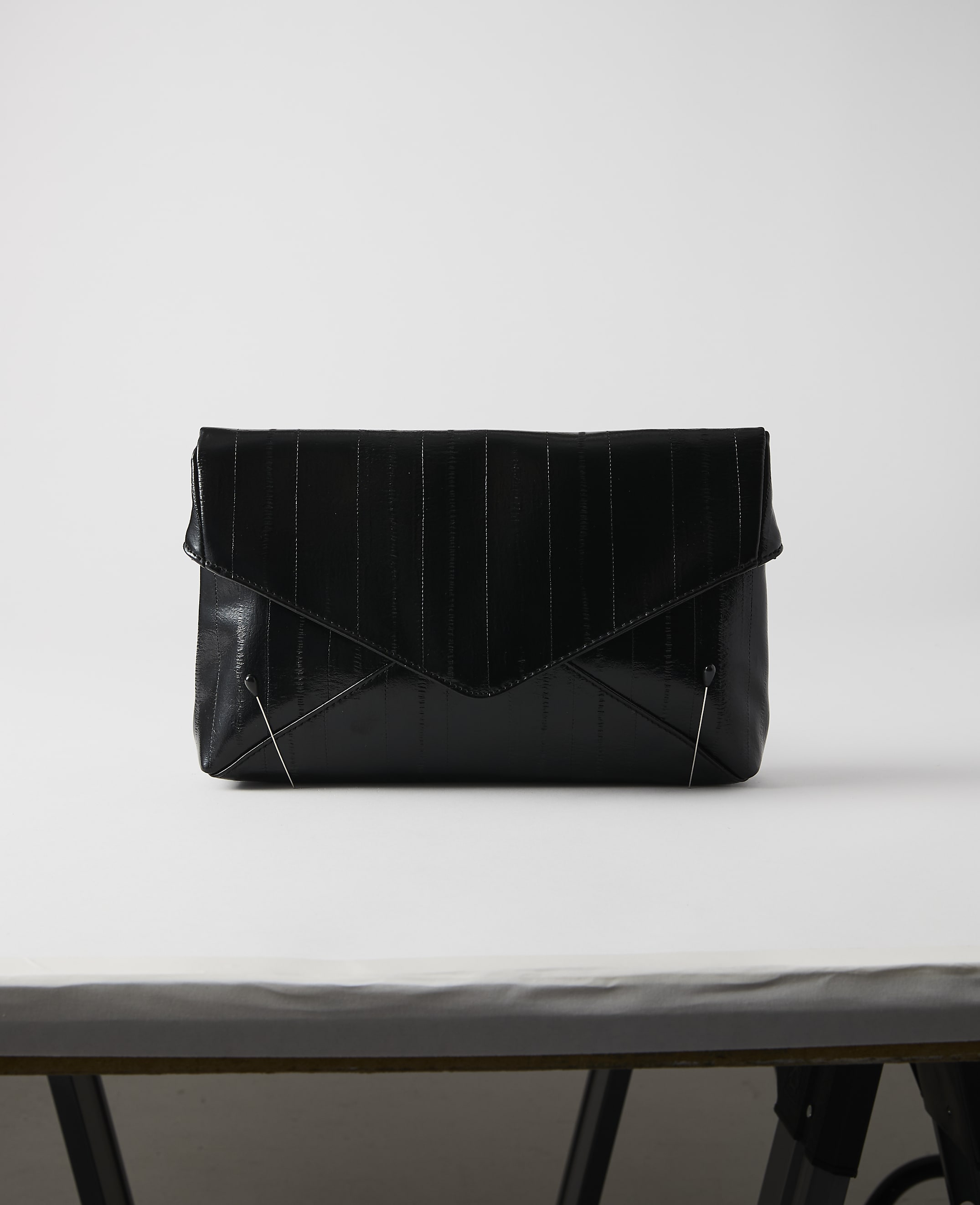 A black, textured envelope clutch rests on a white surface against a plain white background.