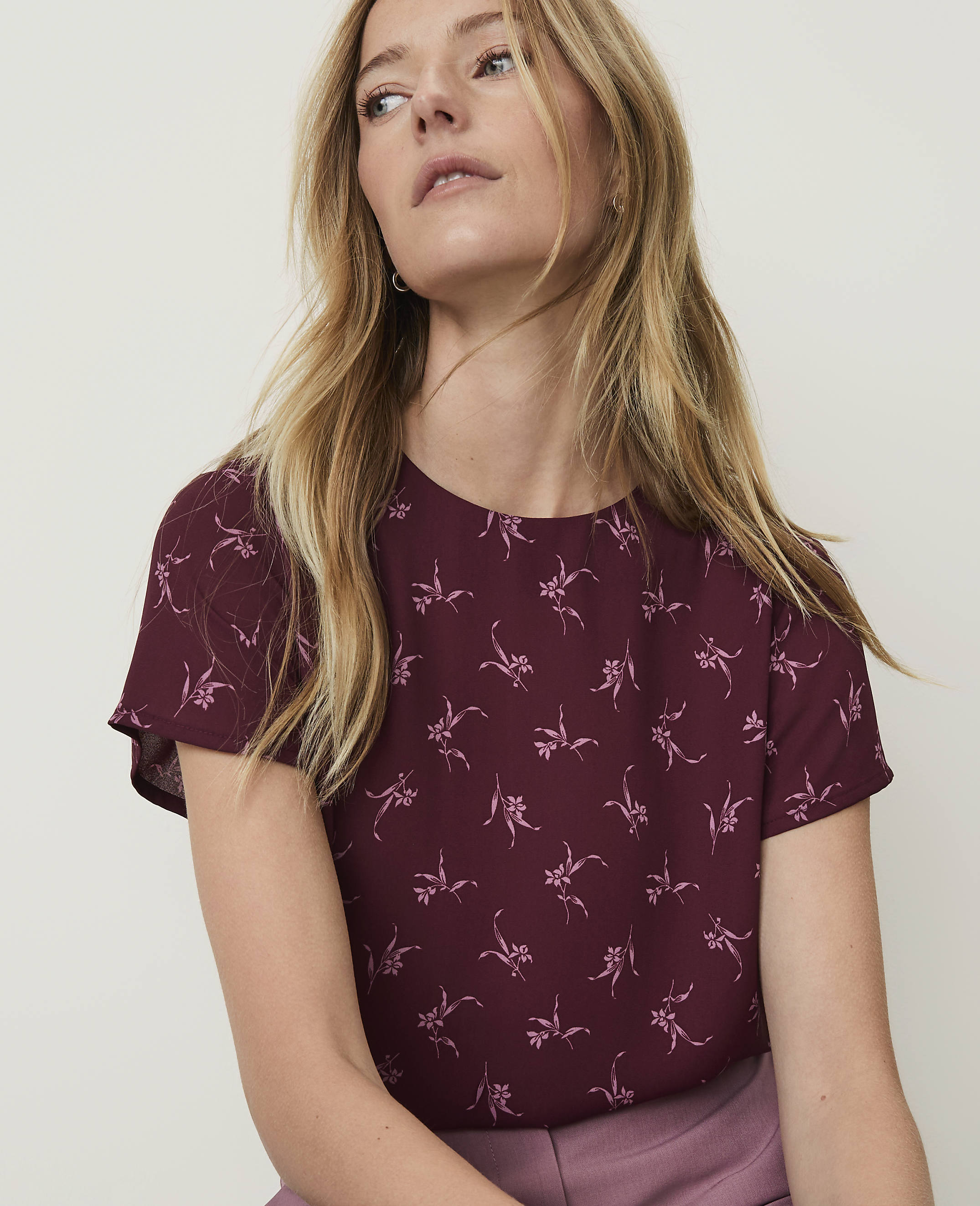 A woman with blonde hair wearing a maroon floral top is shown against a plain background.