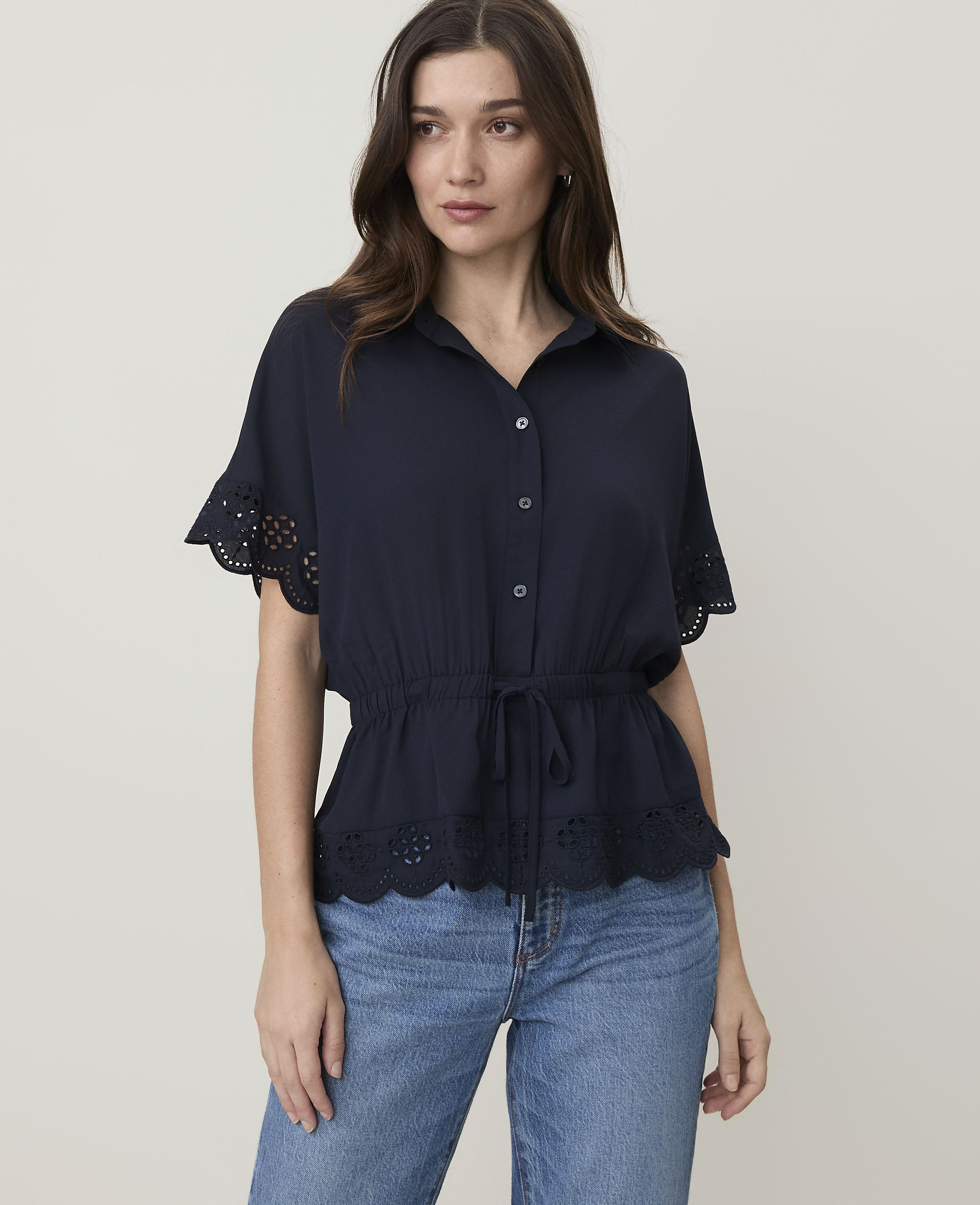 A woman in a navy blue blouse and jeans stands against a plain, light-colored background.