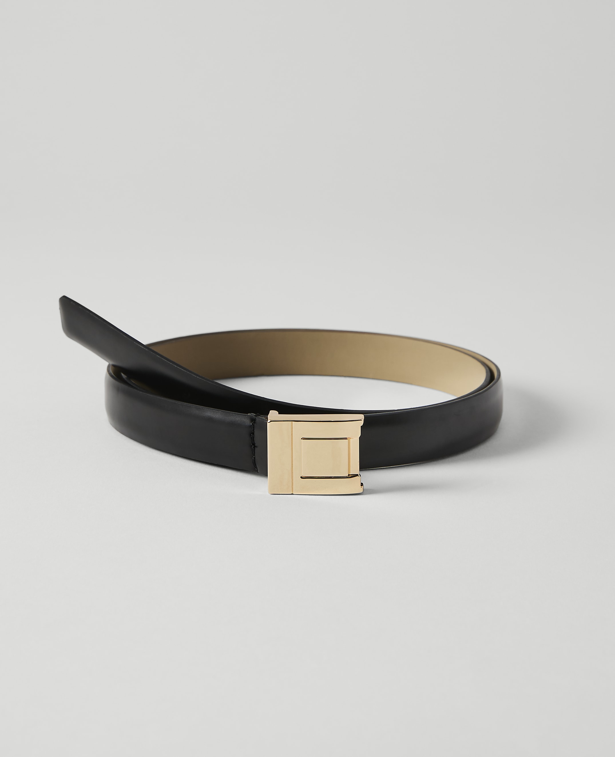A black leather belt with a gold buckle lies on a plain white background.