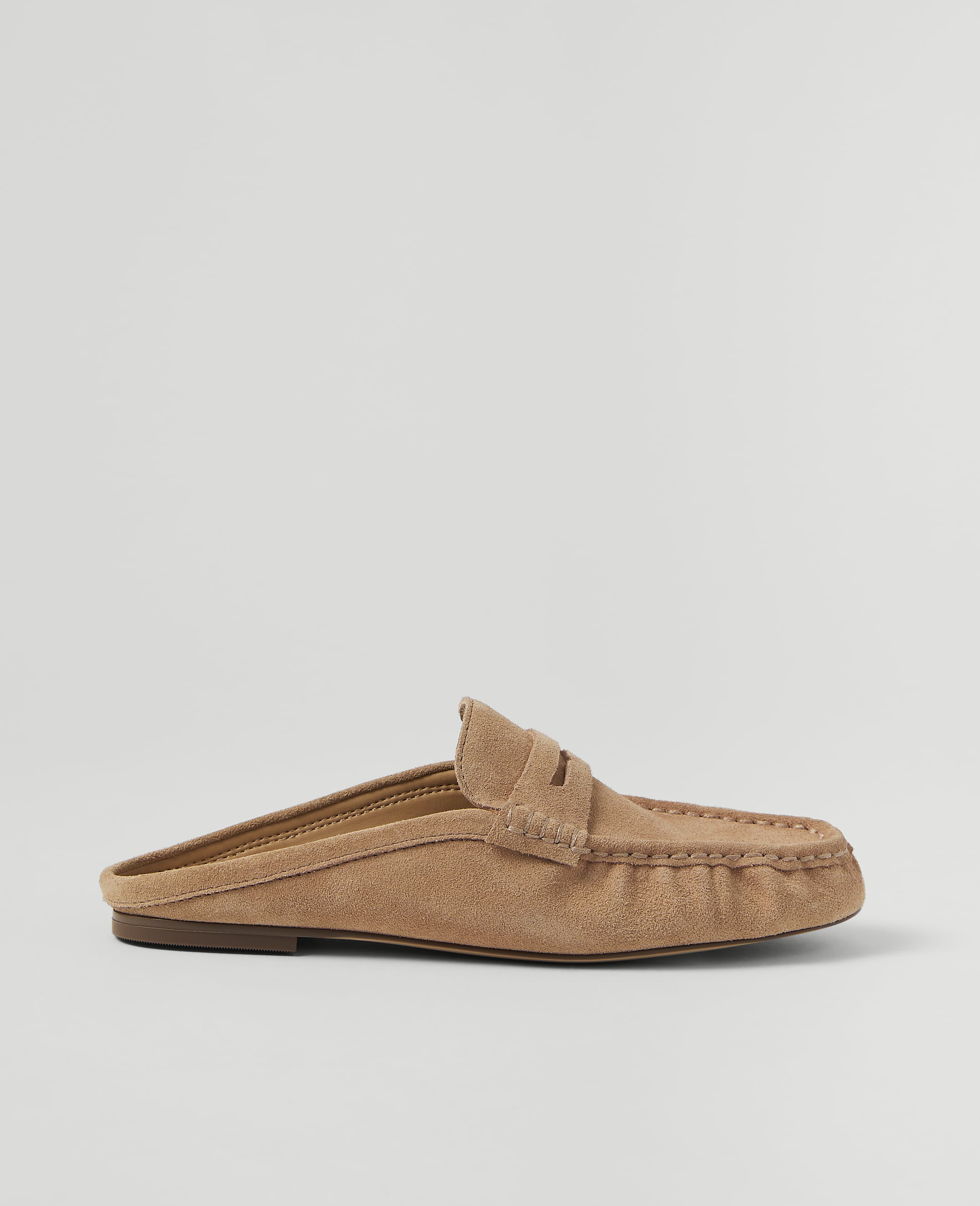 A tan suede mule loafer rests on a plain, light gray background.