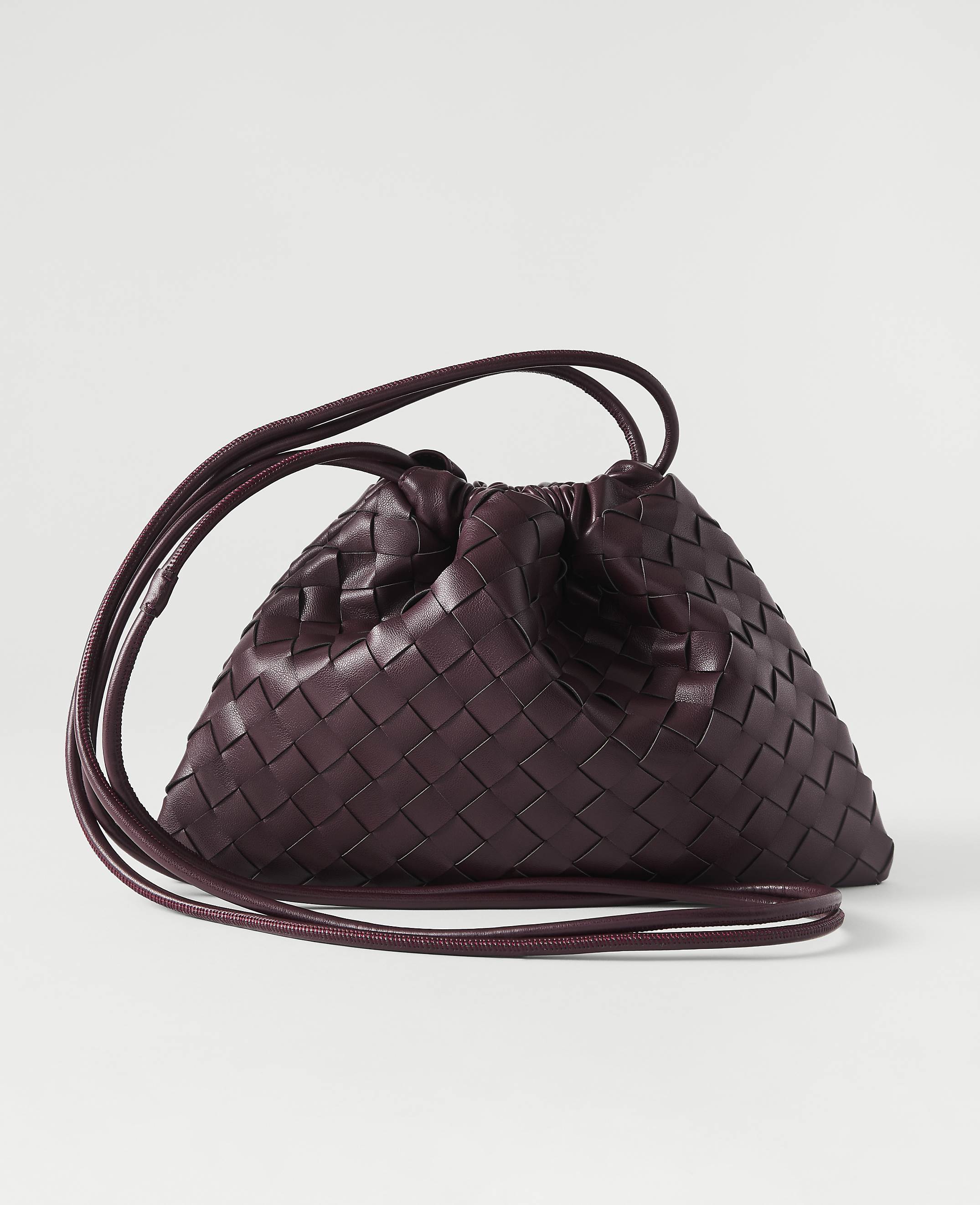 A deep plum, woven leather pouch bag with thin straps rests on a plain white background.