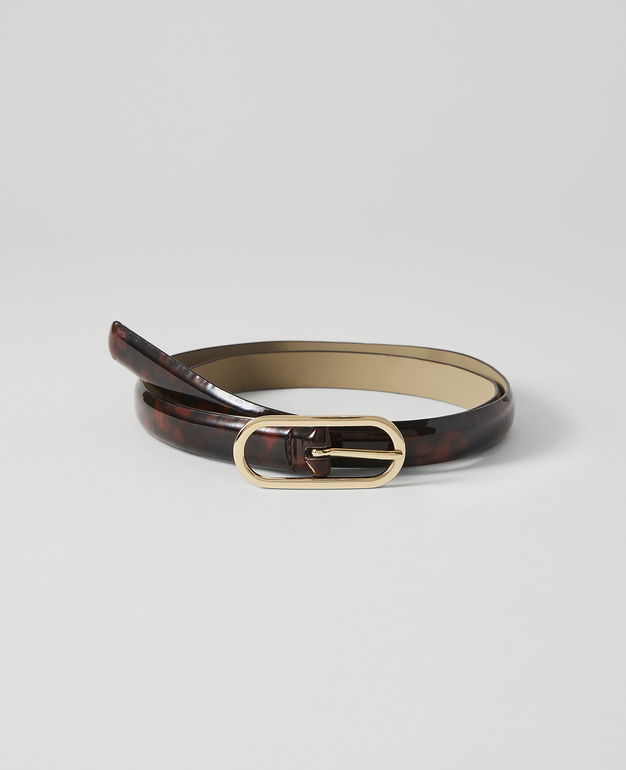 A glossy, tortoiseshell-patterned belt with a gold oval buckle lies coiled on a plain white background.