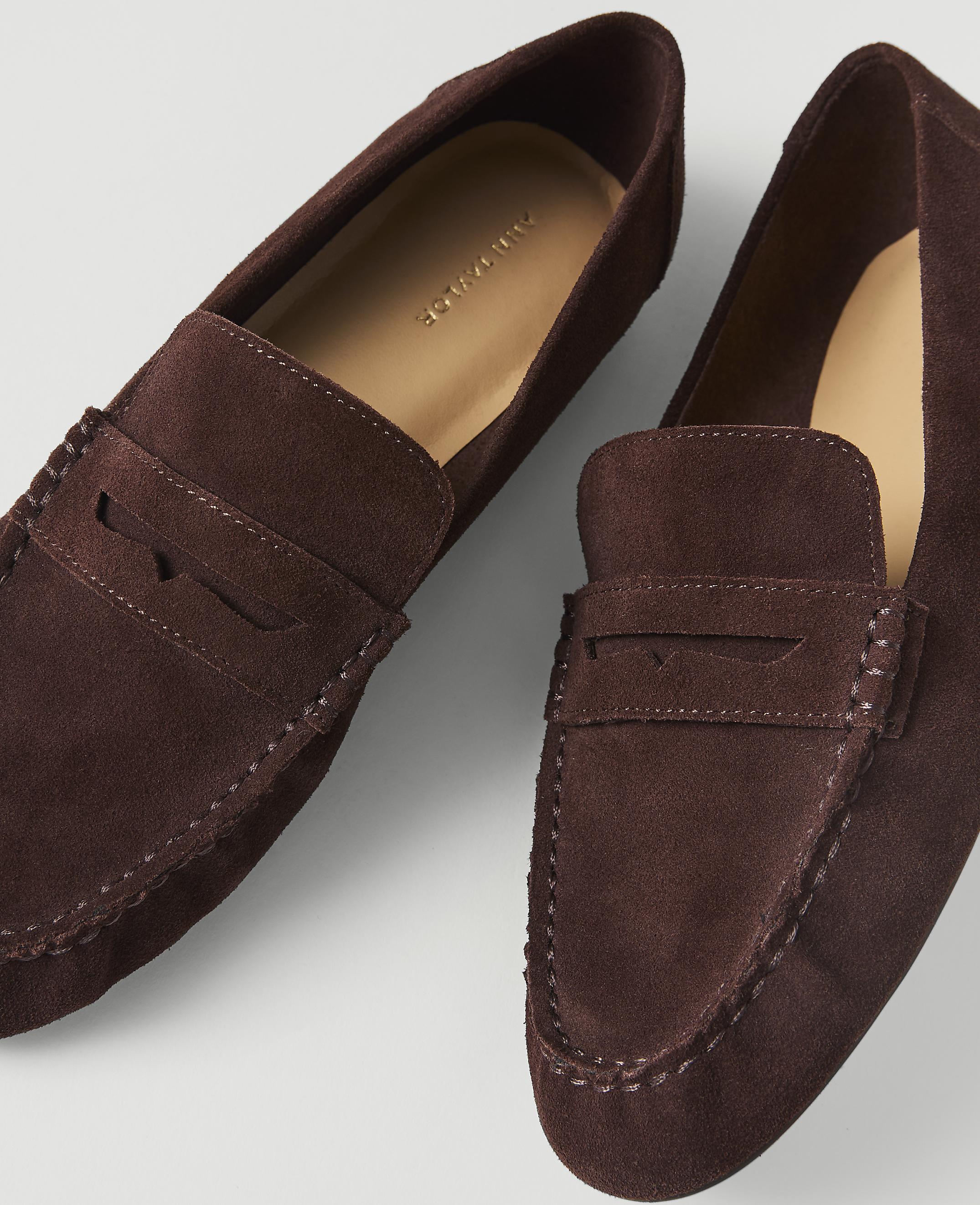 A pair of dark brown suede loafers with visible stitching rests on a plain white background.