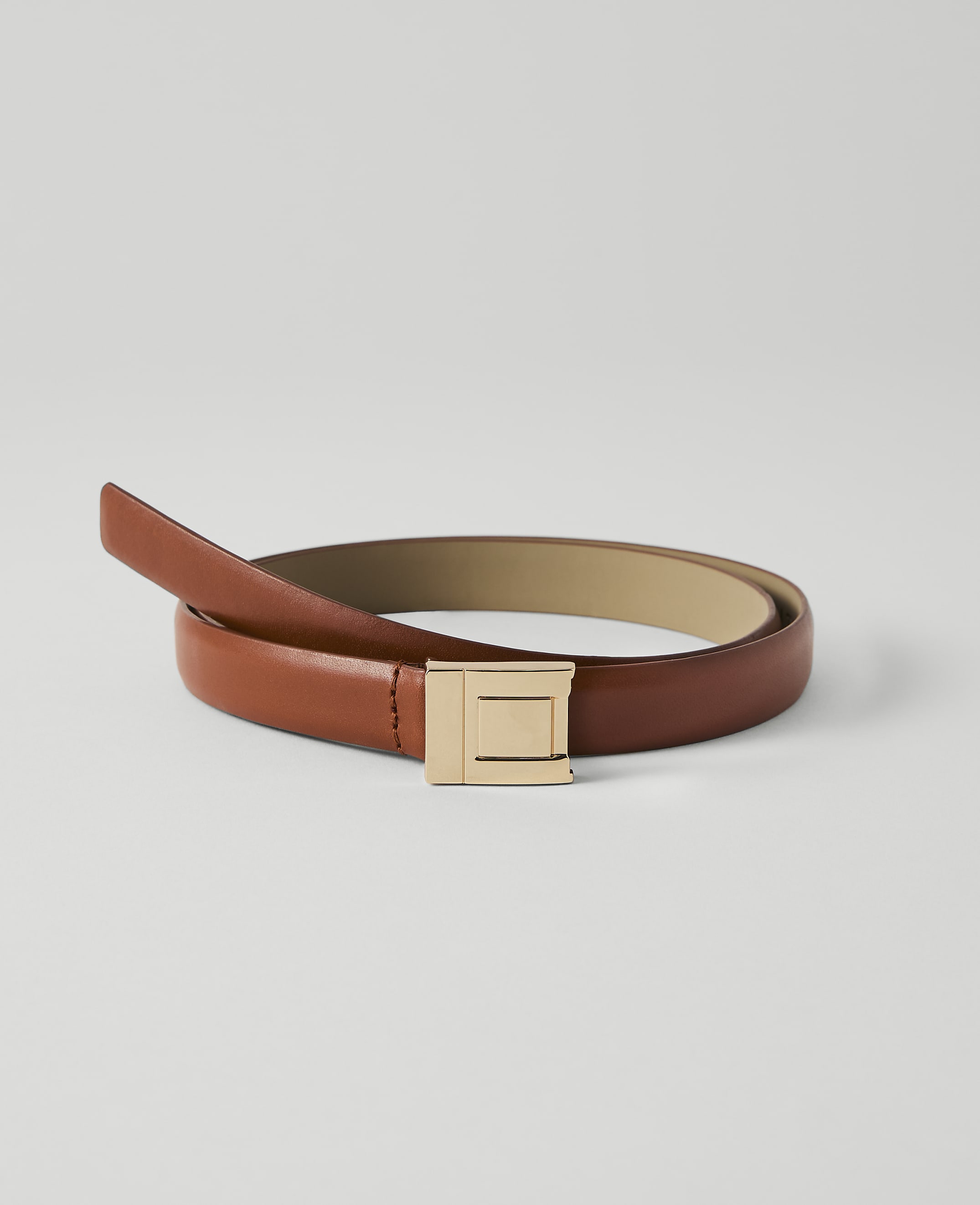 A brown leather belt with a gold buckle lies on a plain white background.