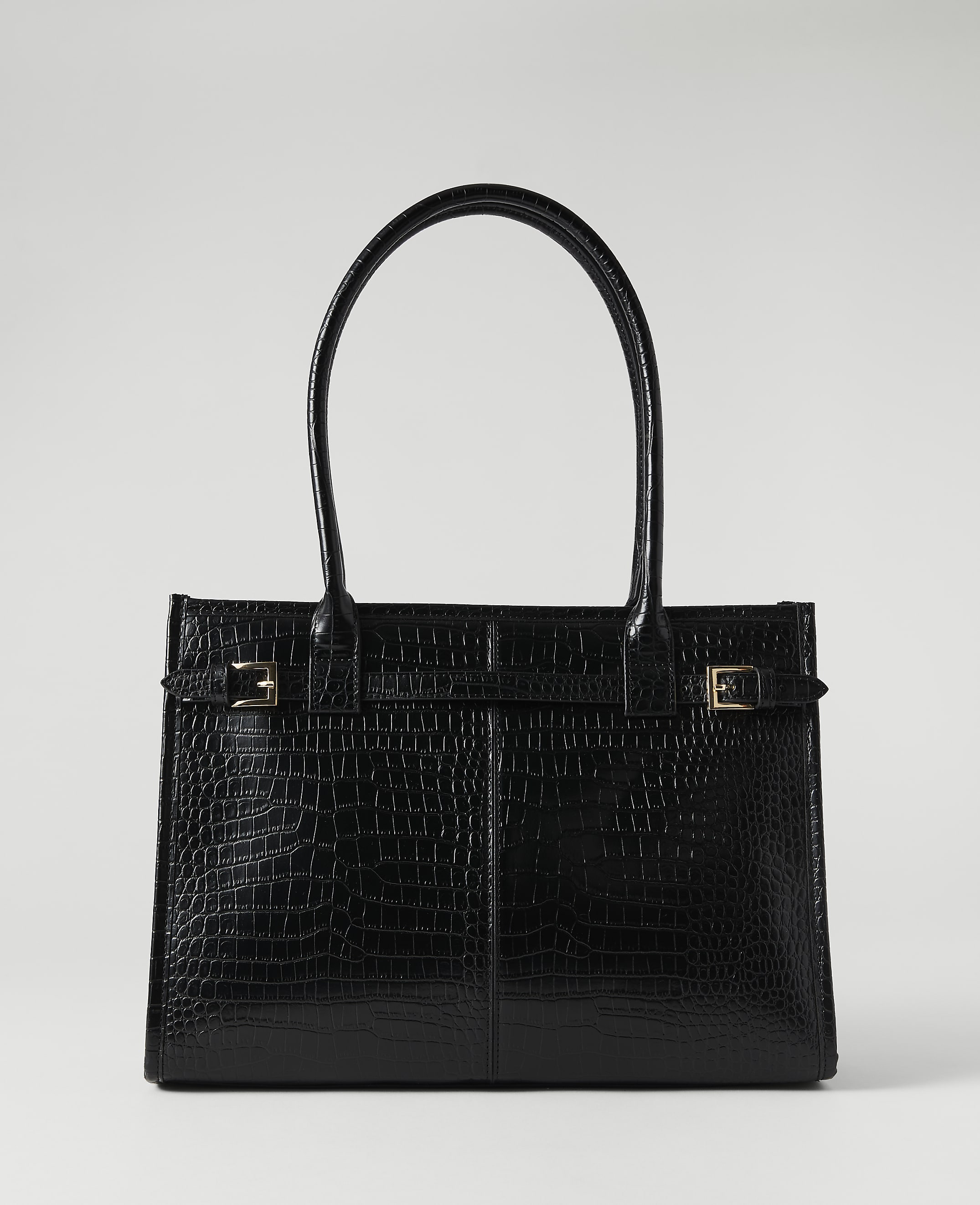 A black crocodile-embossed tote bag with gold buckle accents sits against a plain, light gray background.