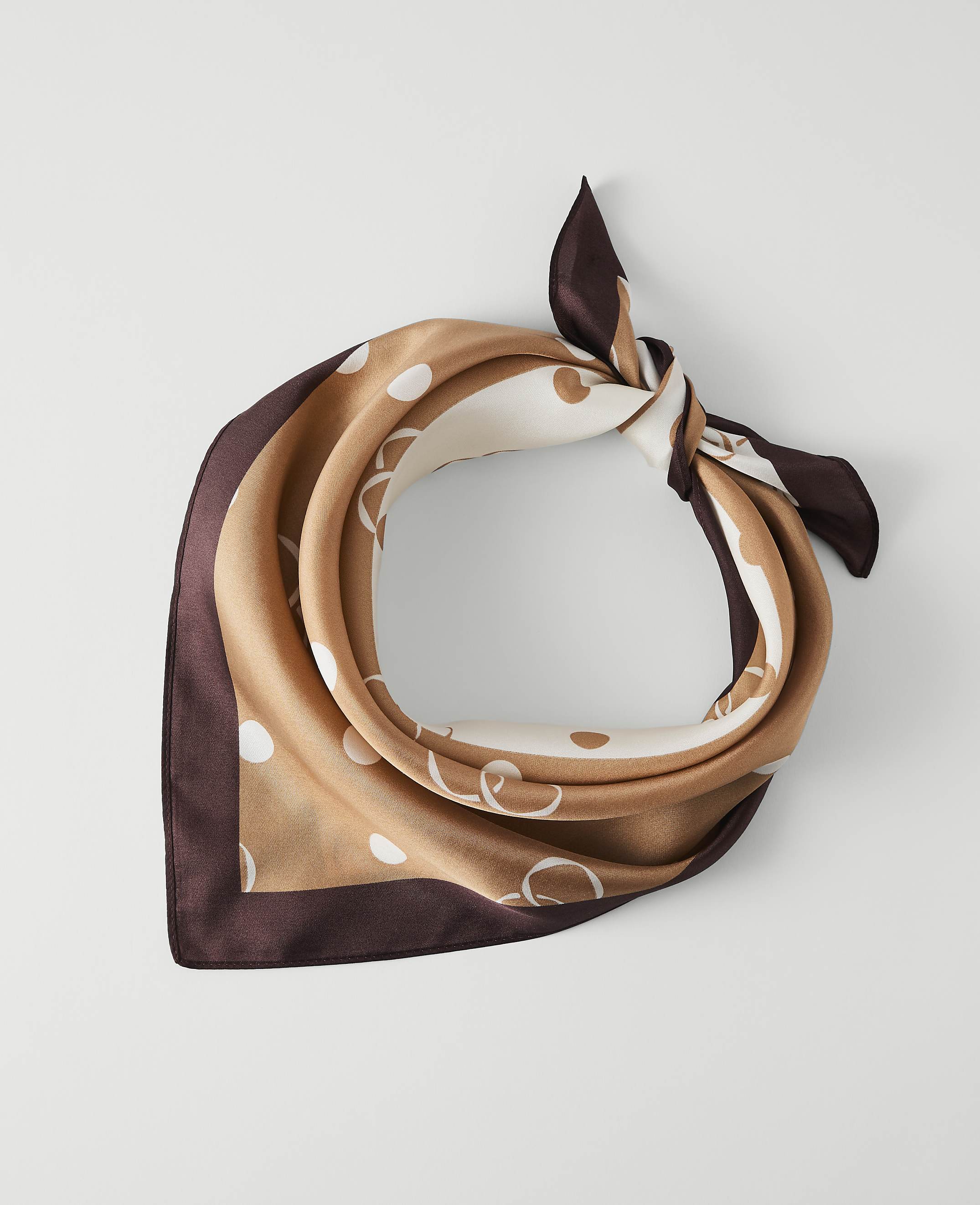 A silk scarf with a polka dot and chain pattern is tied in a knot against a plain white background.