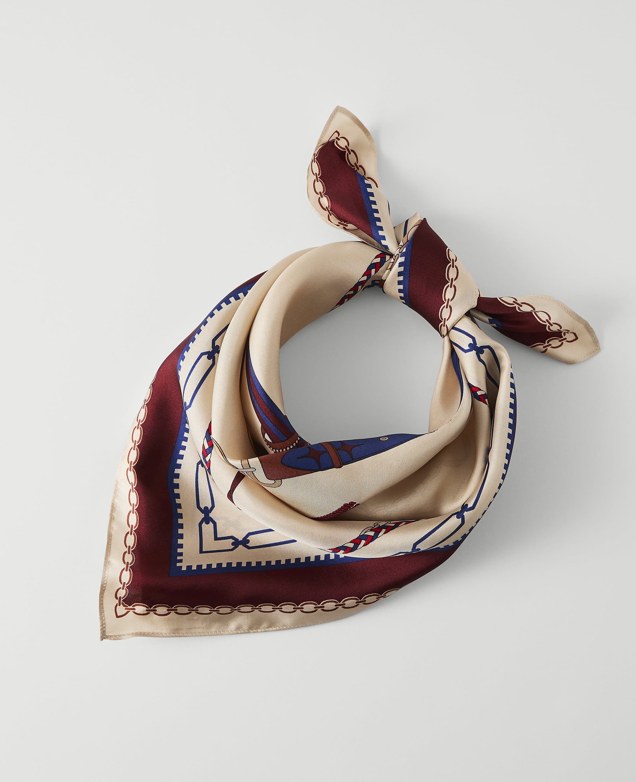 A cream-colored silk scarf with a maroon and blue chain link pattern is laid flat against a plain white background.