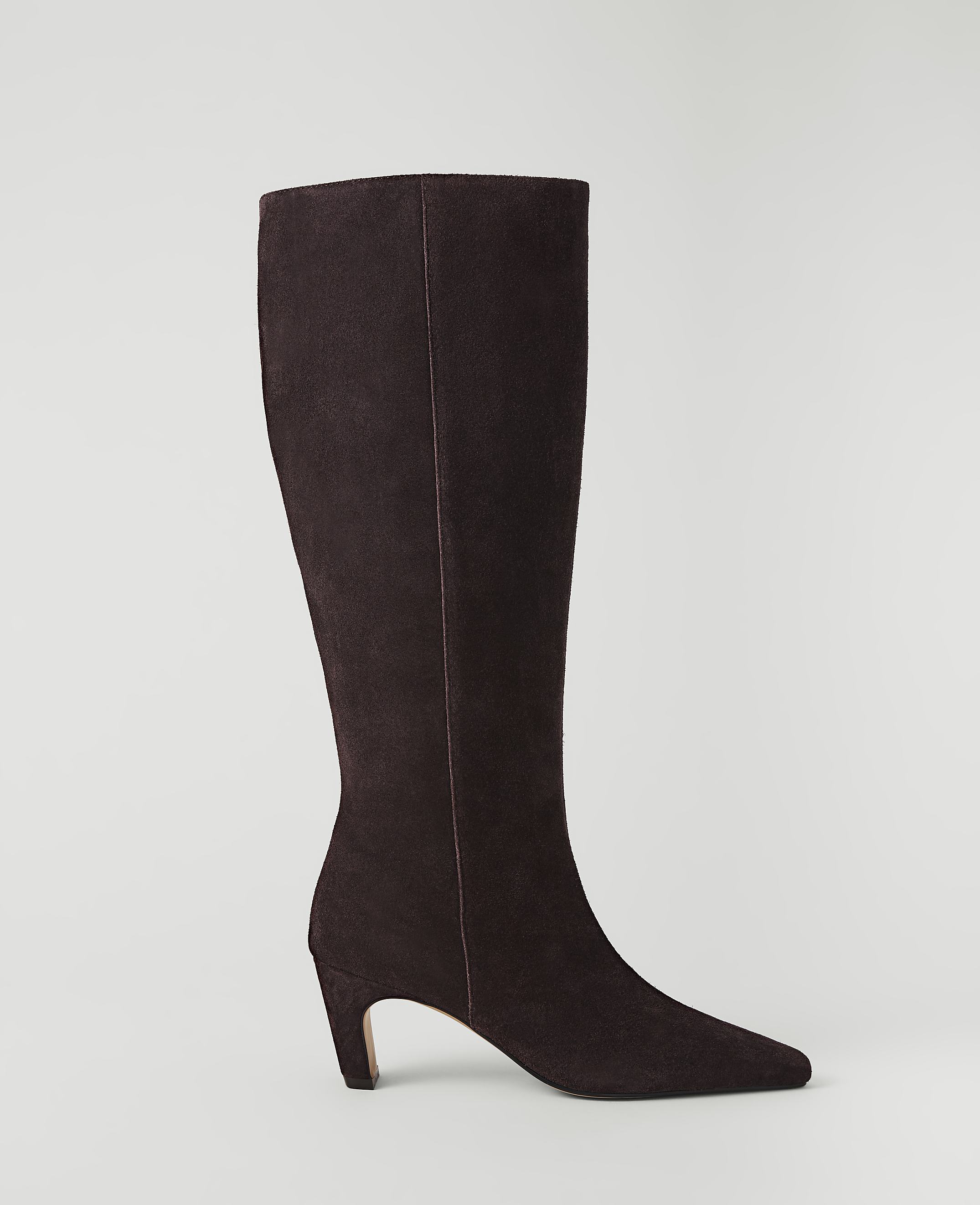 A dark brown suede knee-high boot with a pointed toe and a curved heel stands against a plain, light gray background.