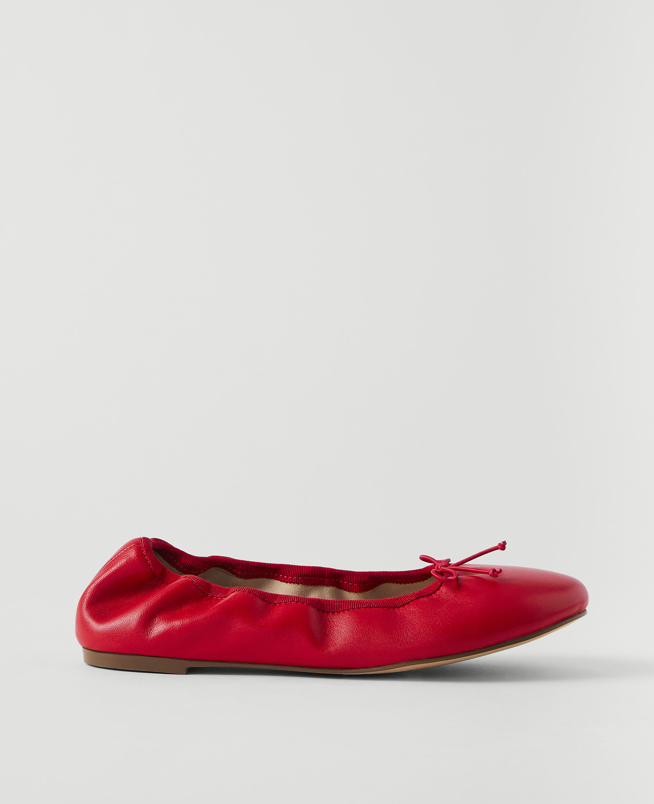 A red leather ballet flat with a bow sits on a plain white background.