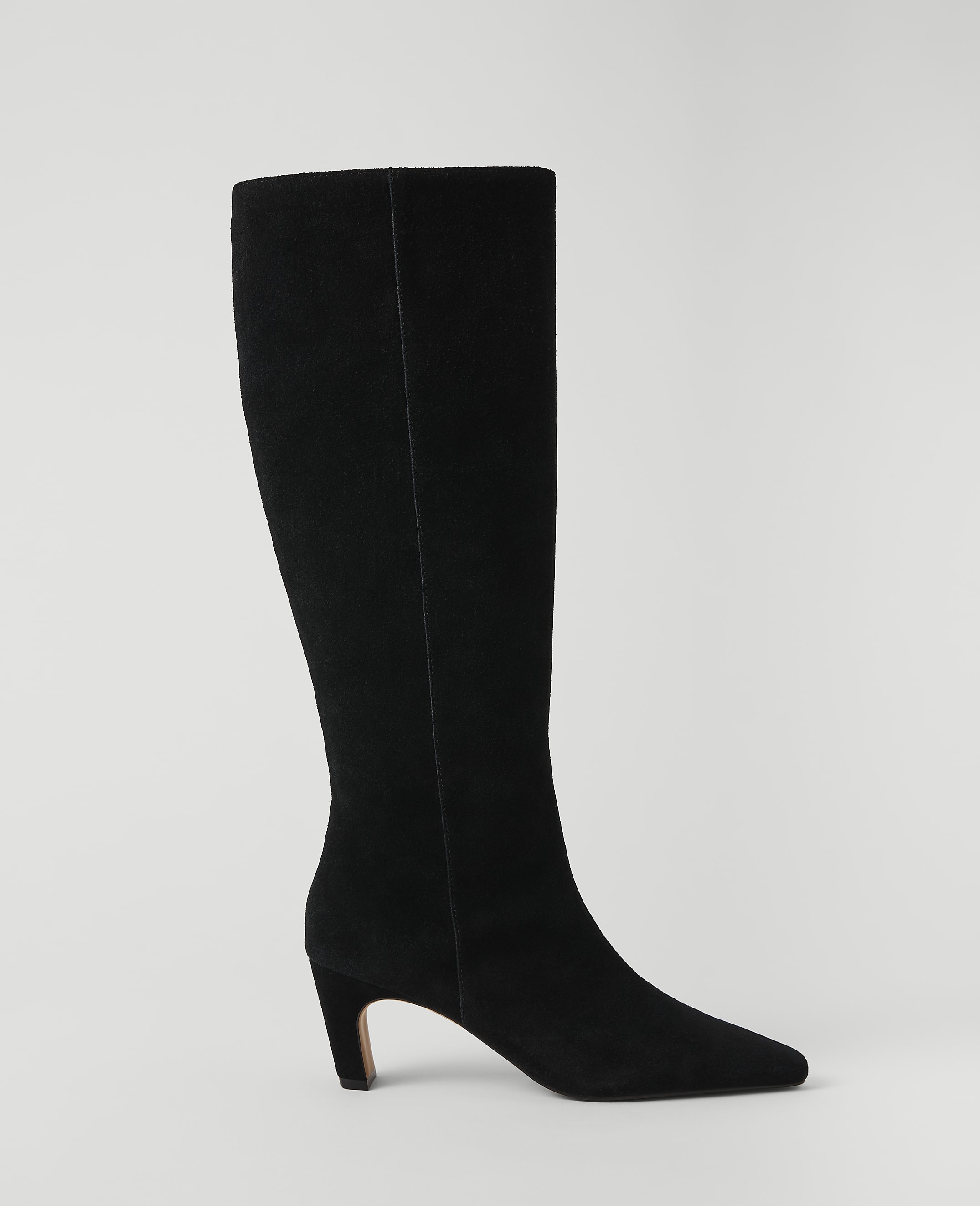 A black suede knee-high boot with a pointed toe and a low heel stands against a plain white background.