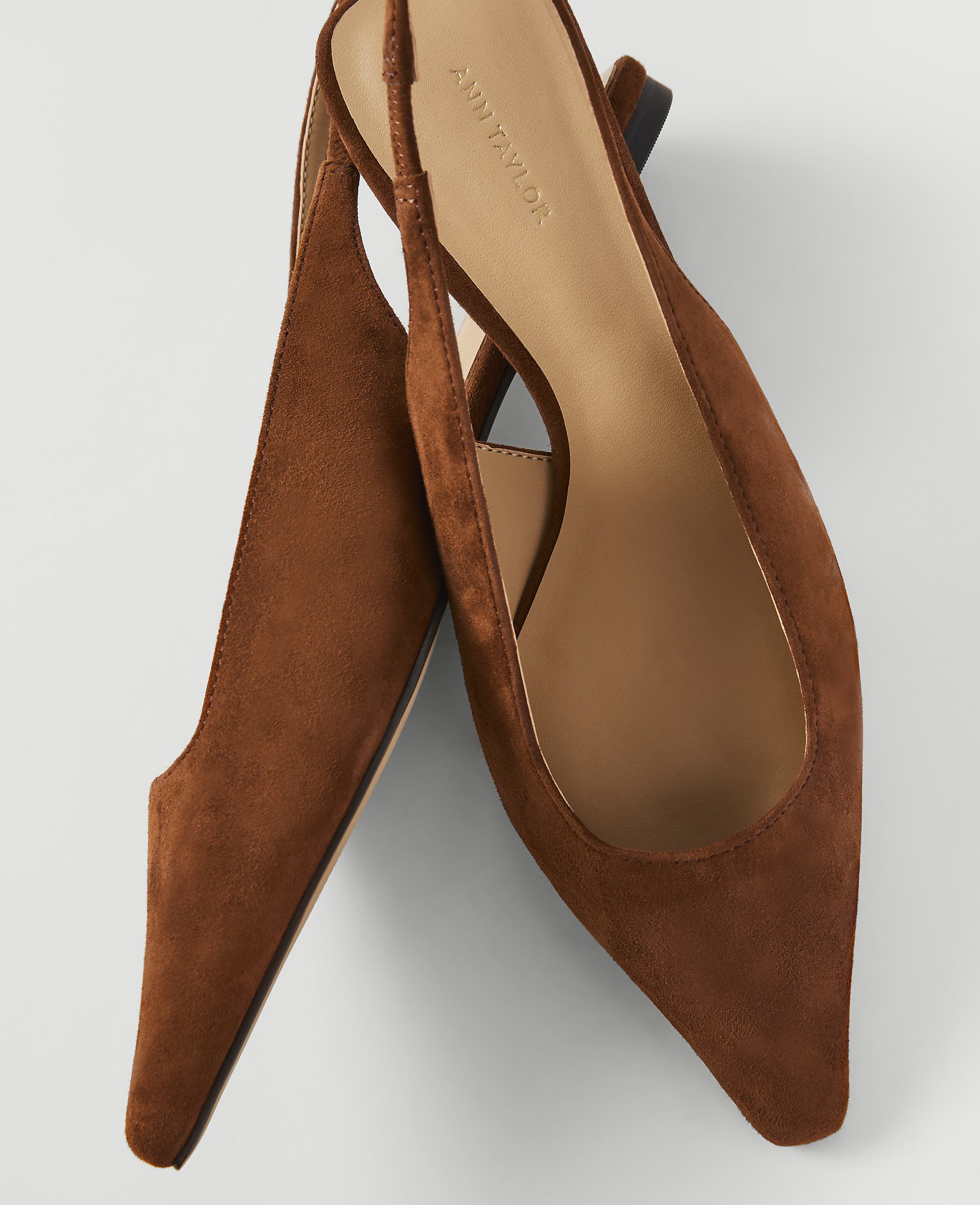 A pair of brown suede slingback heels with pointed toes rests on a plain white background.