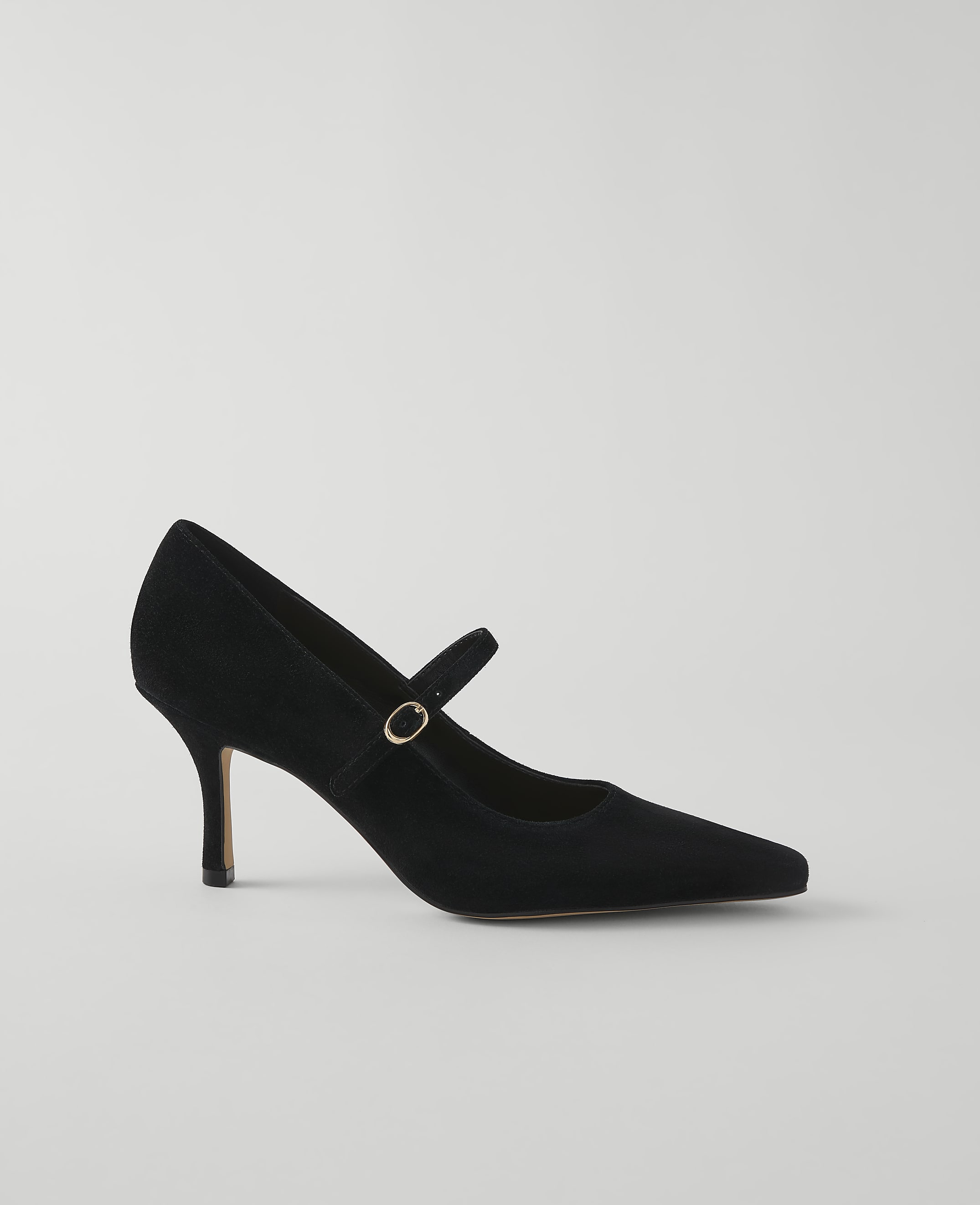 A black suede Mary Jane pump with a pointed toe and a thin heel rests on a plain, light gray background.