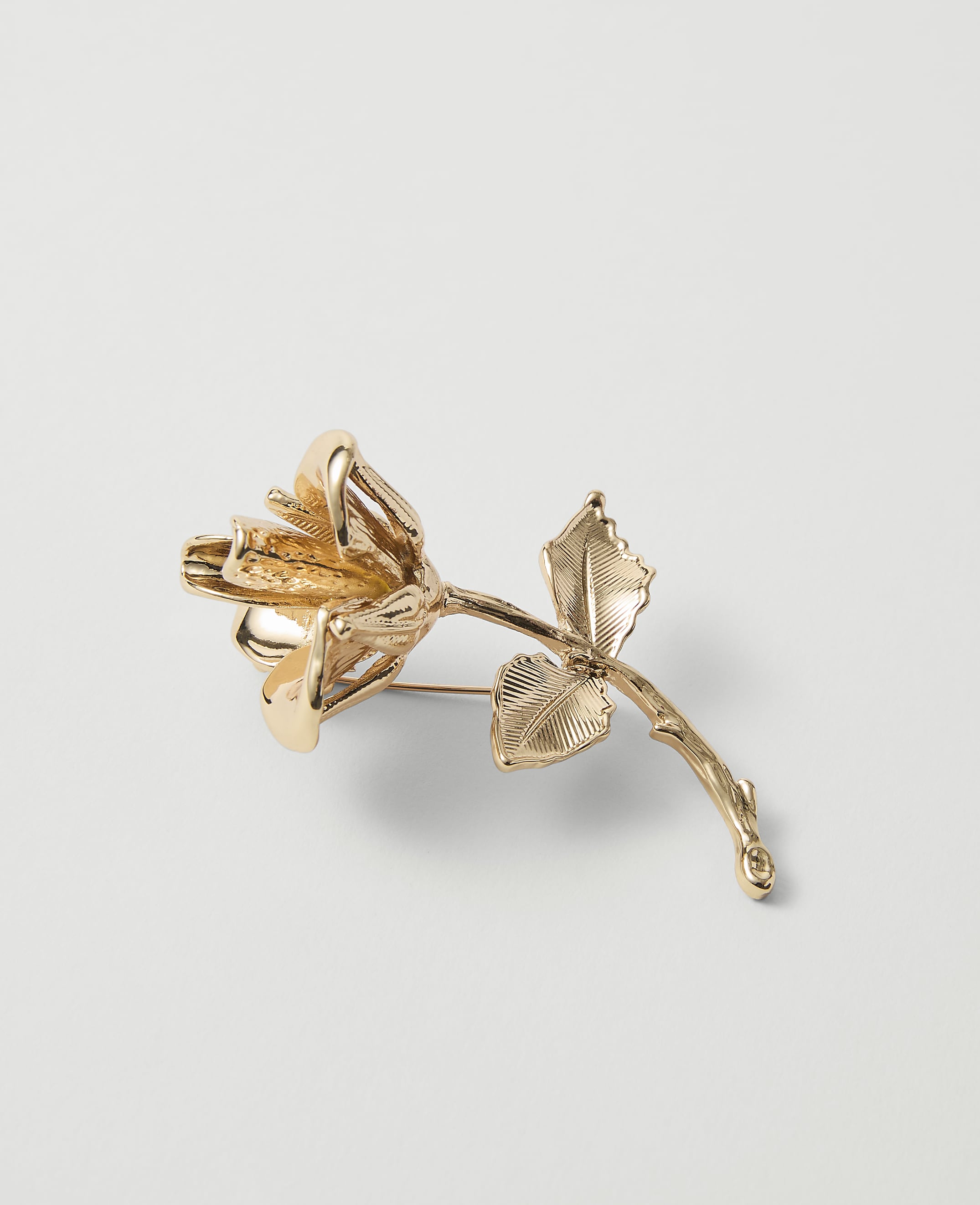 A golden rose brooch with detailed petals and leaves rests on a plain white background.