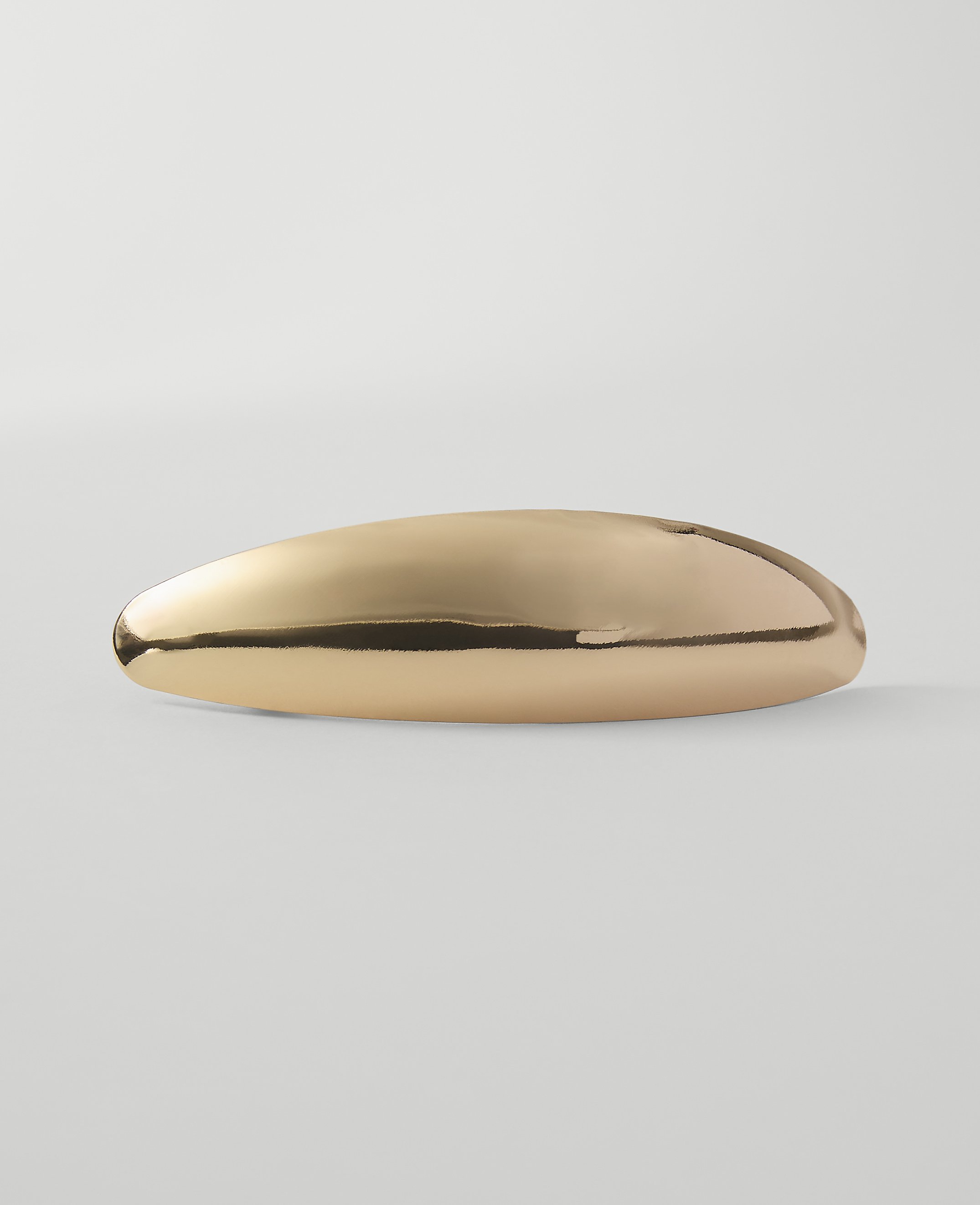 A polished, elongated gold object rests on a plain, light gray surface against a soft, white background.
