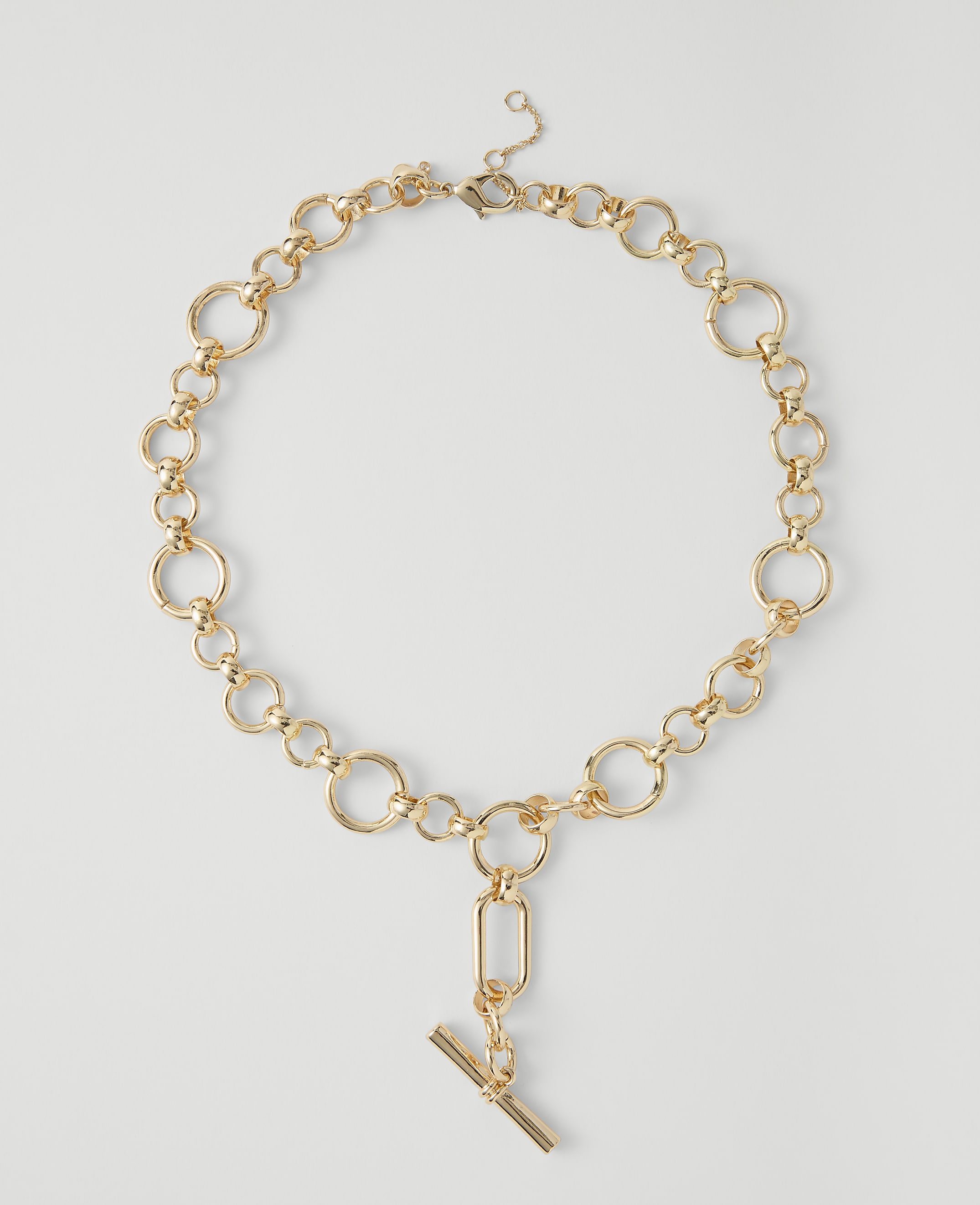 A gold chain necklace with a toggle clasp and pendant rests on a plain white background.